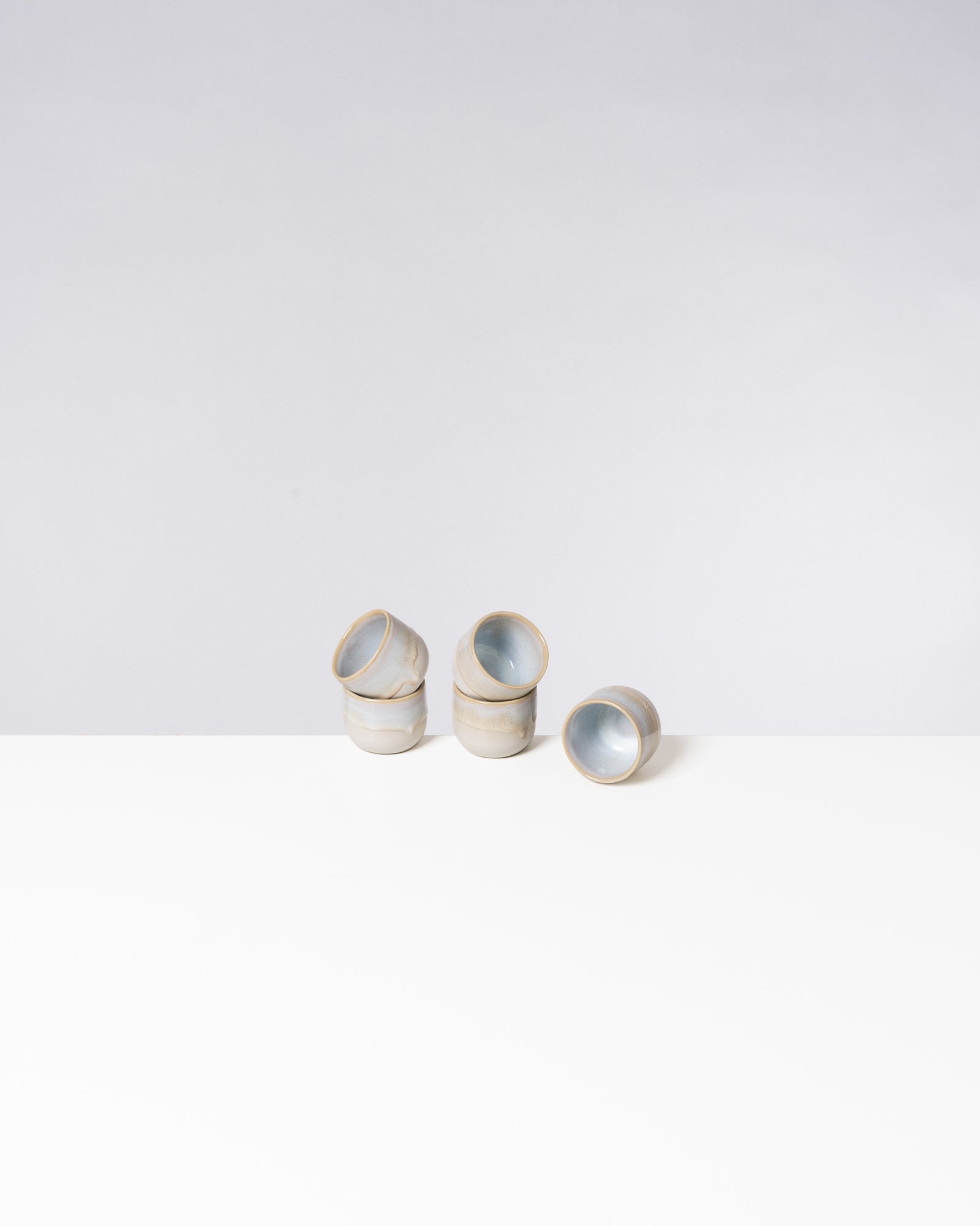 Fünf gestapelte Keramikbecher mit blau-grauem Inneren auf einem weißen Tisch vor grauem Hintergrund.