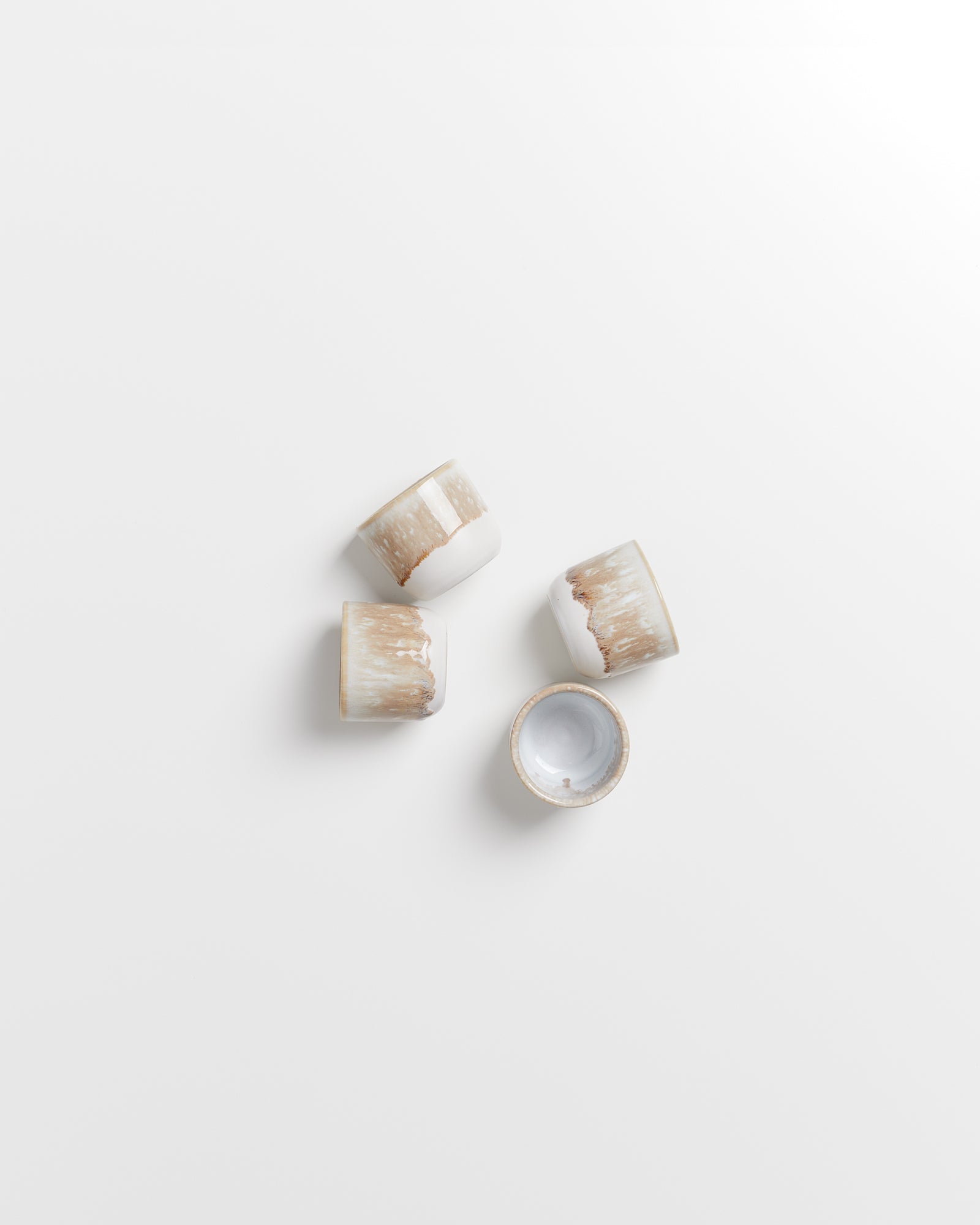 Vier kleine, weiß-braune Keramikschalen liegen auf einem weißen Hintergrund.