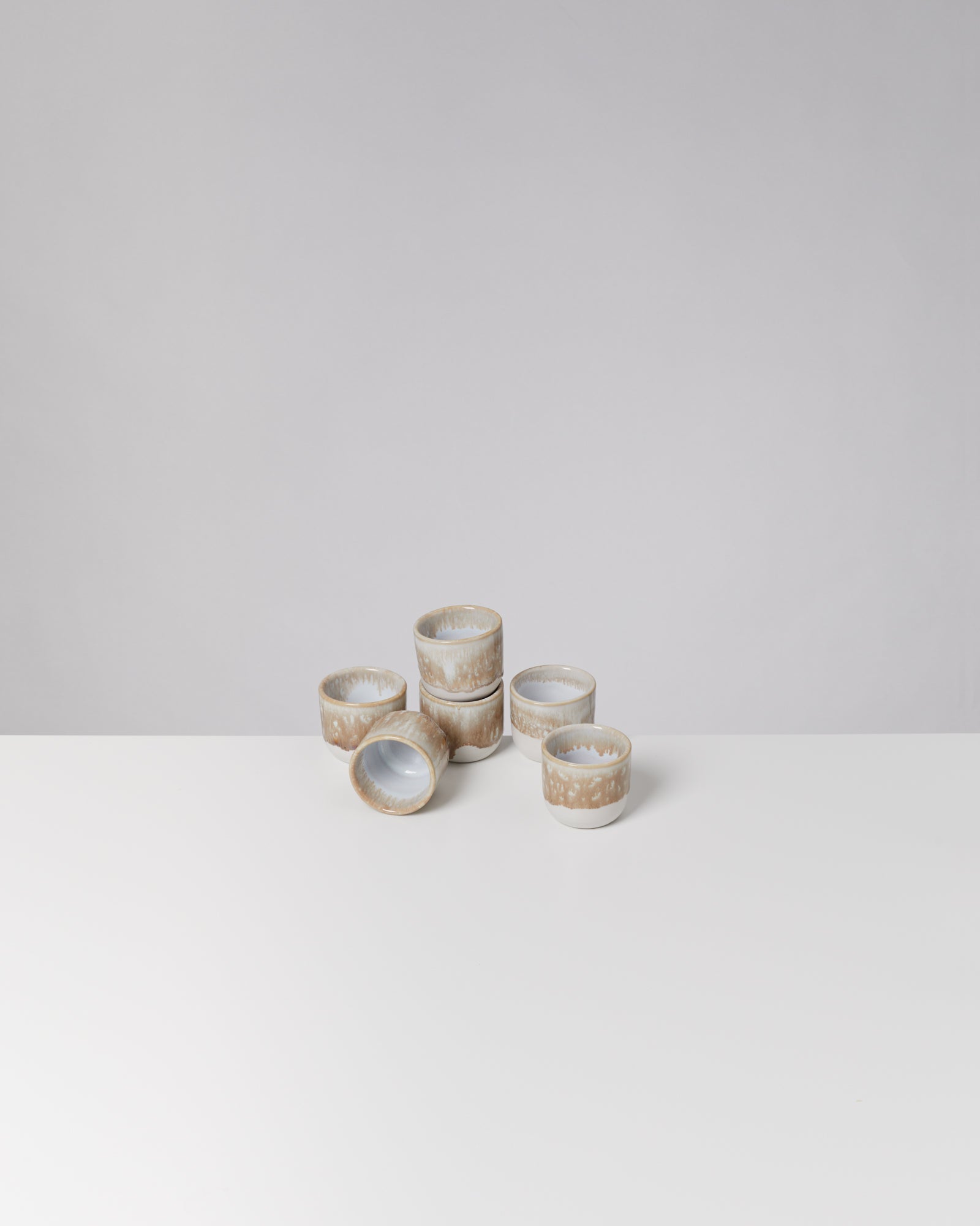 Sechs stapelbare Tassen mit braun-weißem Muster auf einem weißen Tisch vor grauem Hintergrund.