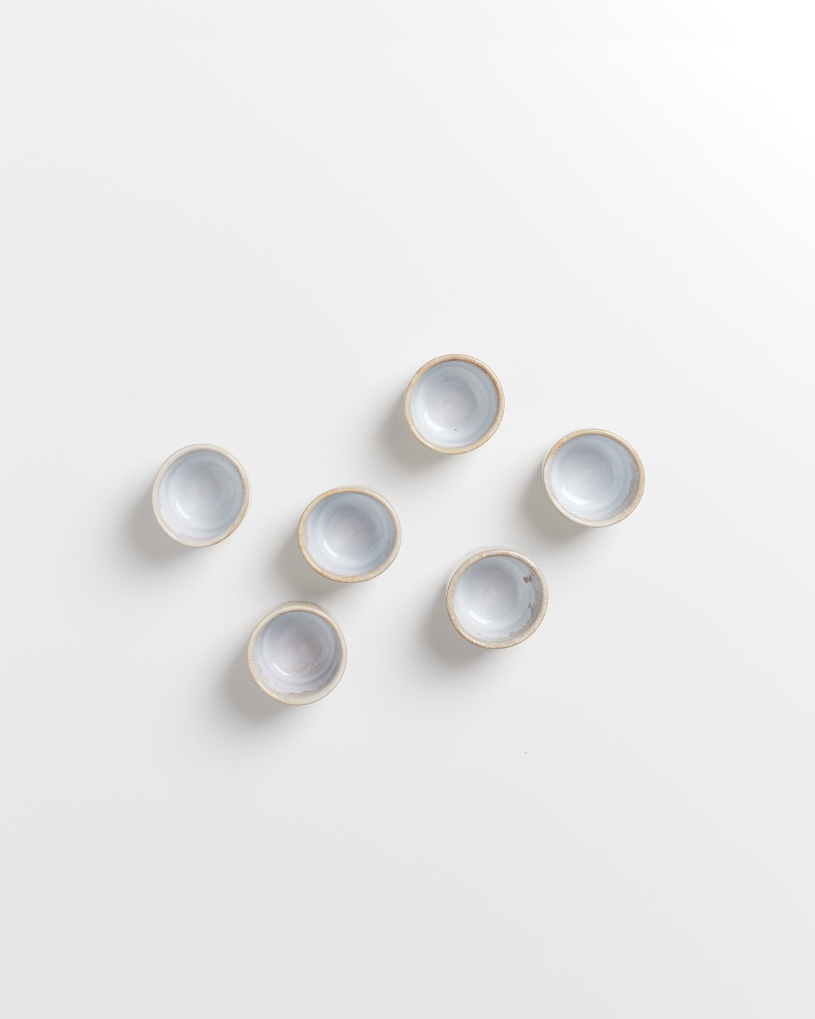 Sechs kleine, runde, weiße Keramikschalen mit hellbraunen Rändern auf weißem Hintergrund.