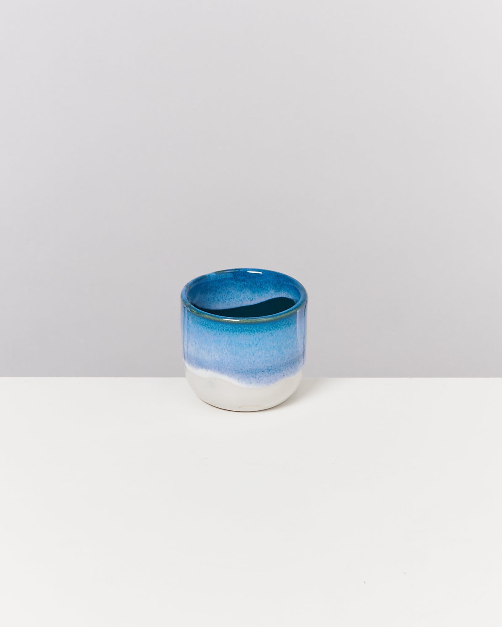 Ein blau-weißer Keramikbecher steht auf einer weißen Oberfläche vor einem grauen Hintergrund.