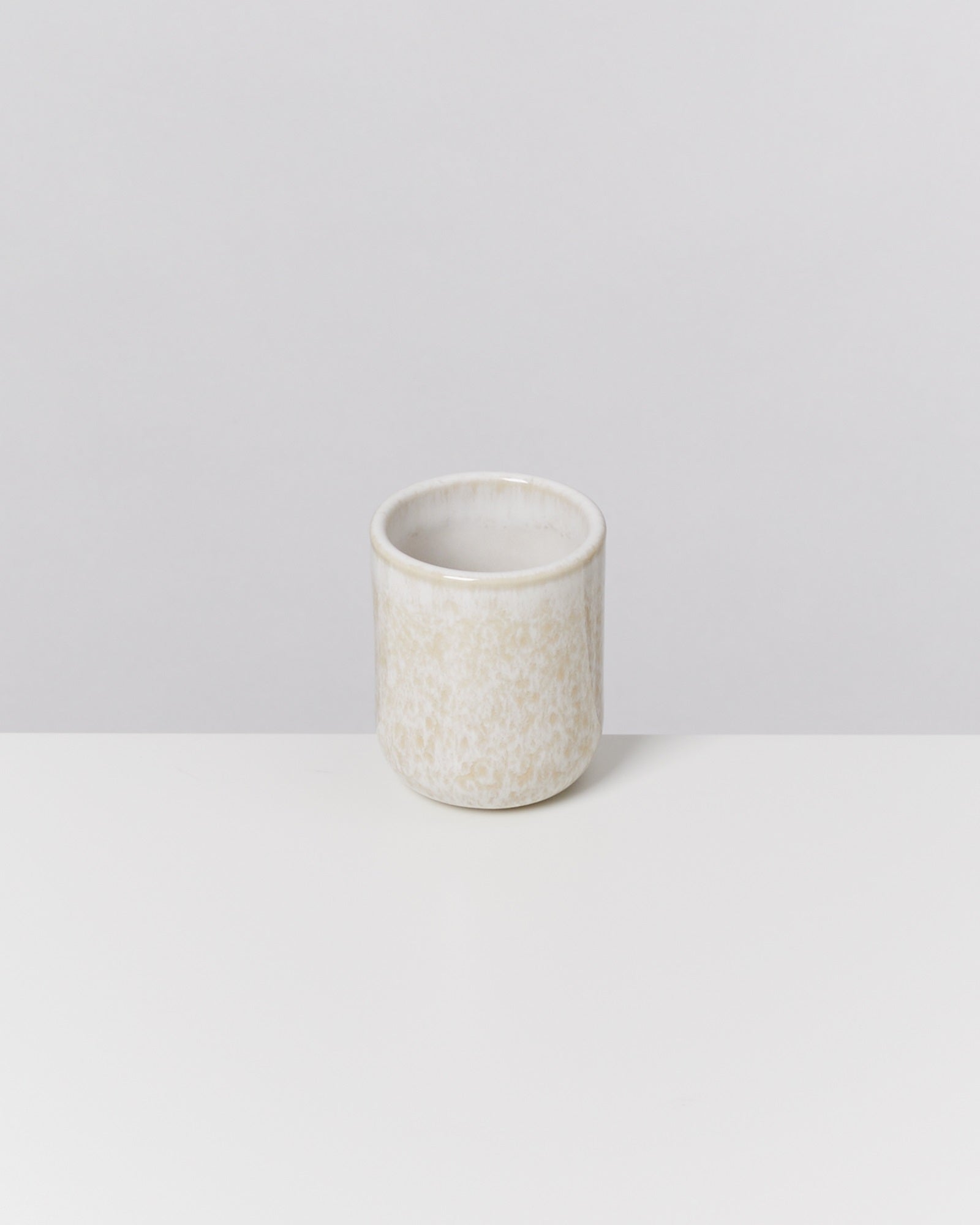 Kleiner, cremefarbener Keramikbecher auf einem weißen Hintergrund.