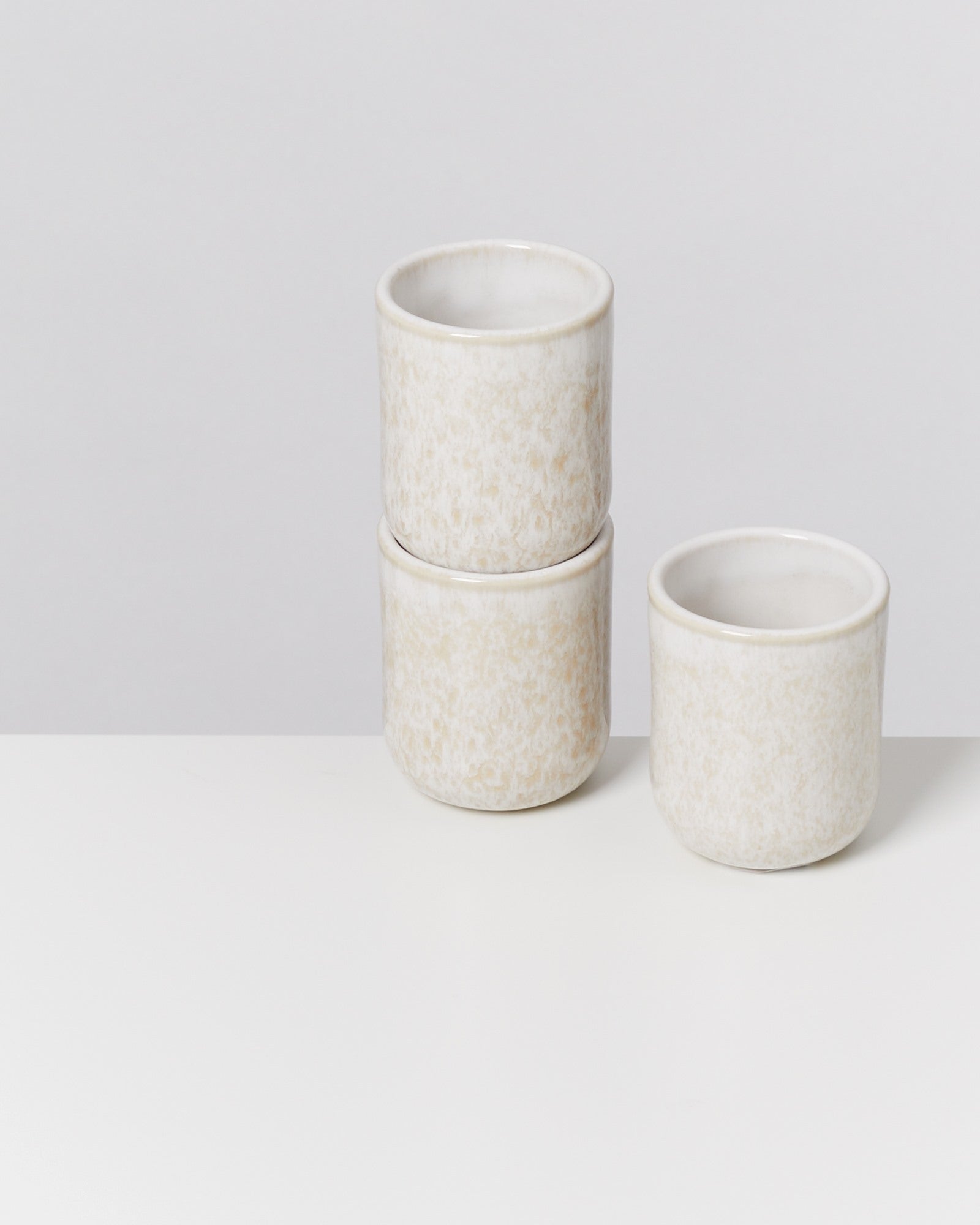 Drei weiße Keramikbecher auf einem weißen Tisch, zwei gestapelt und einer daneben.