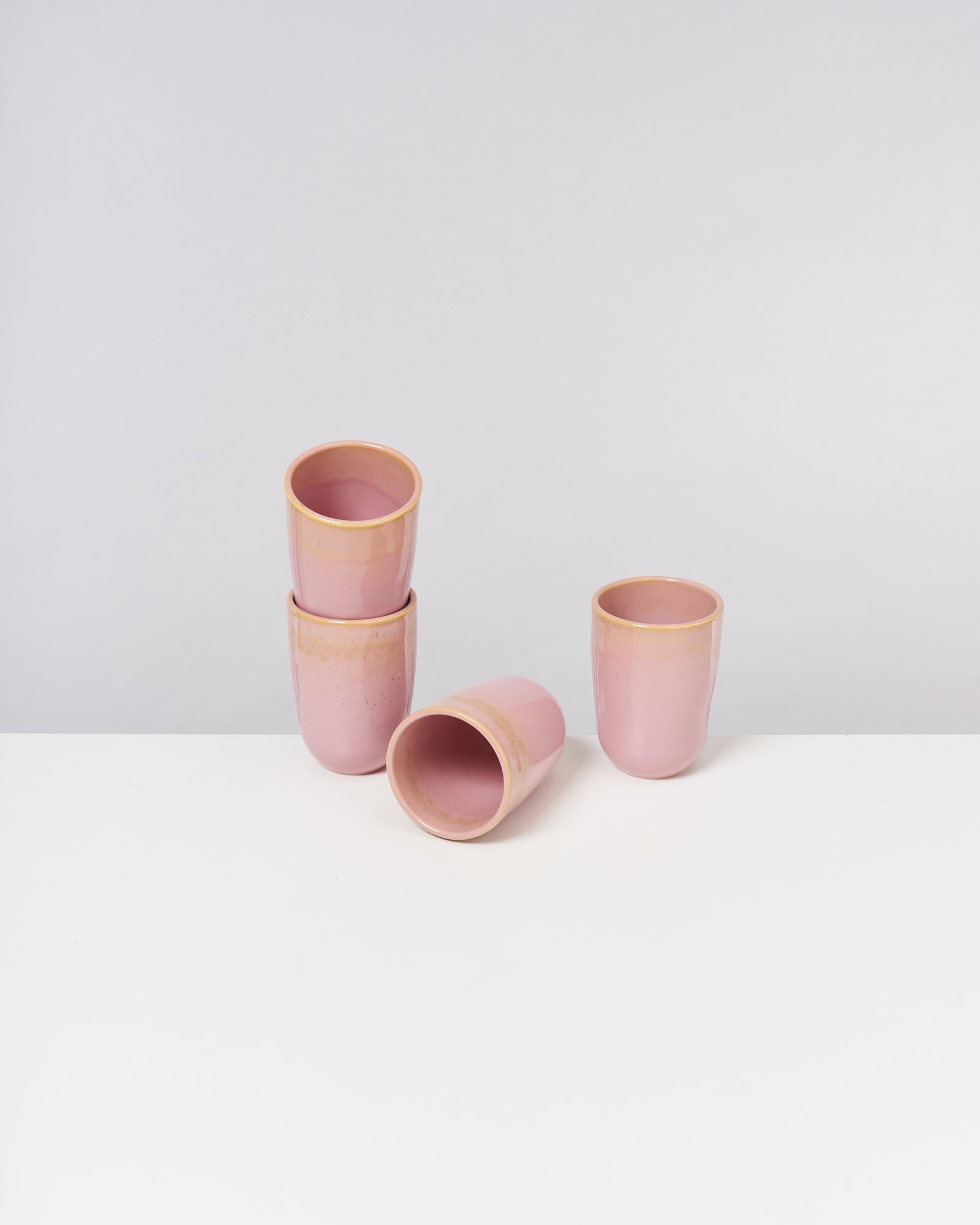 Vier rosafarbene Becher, einer liegend, auf weißem Hintergrund.