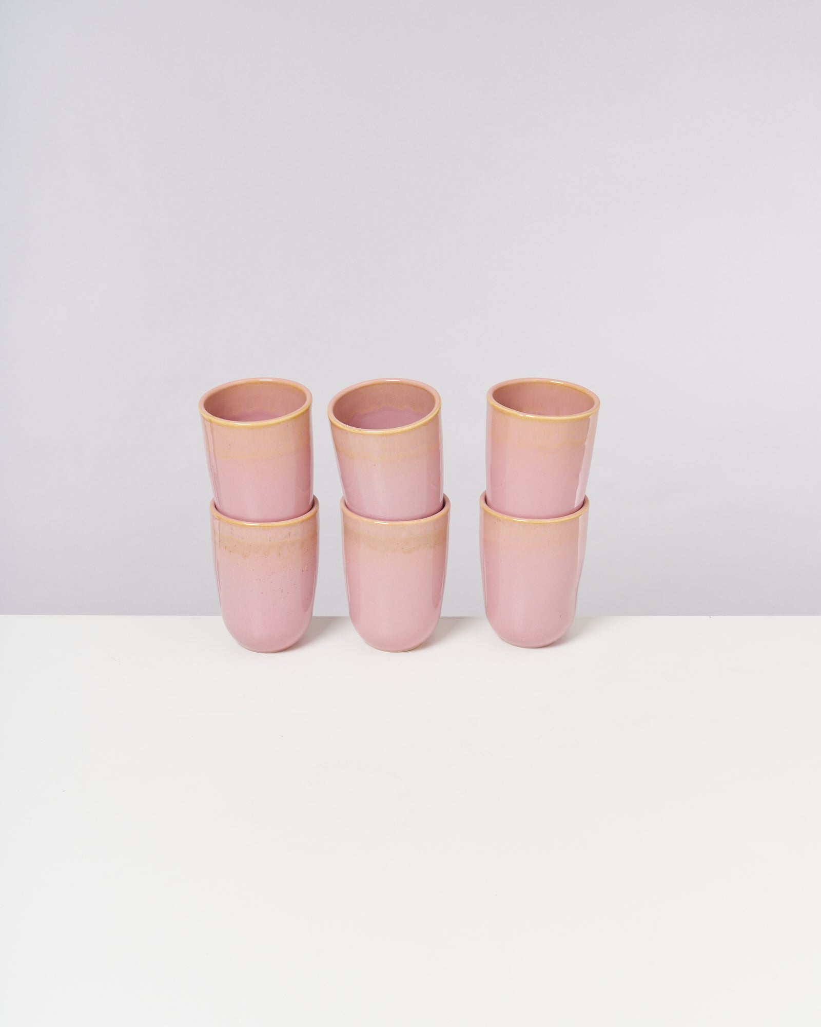 Sechs gestapelte rosa Becher aus Keramik auf einem weißen Tisch vor neutralem Hintergrund.