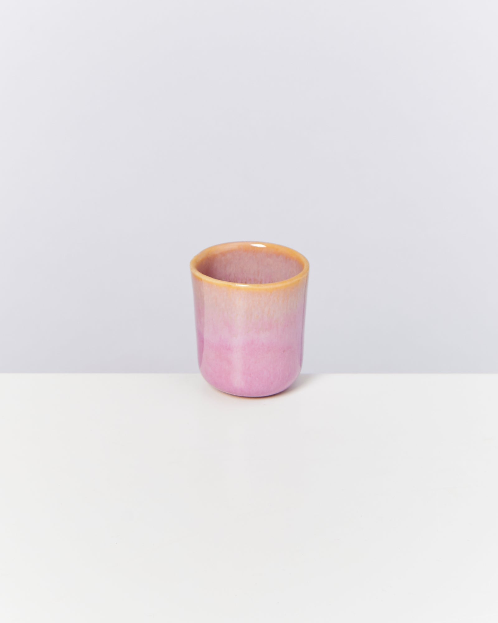 Rosa Keramikbecher mit orangem Rand auf weißem Hintergrund.