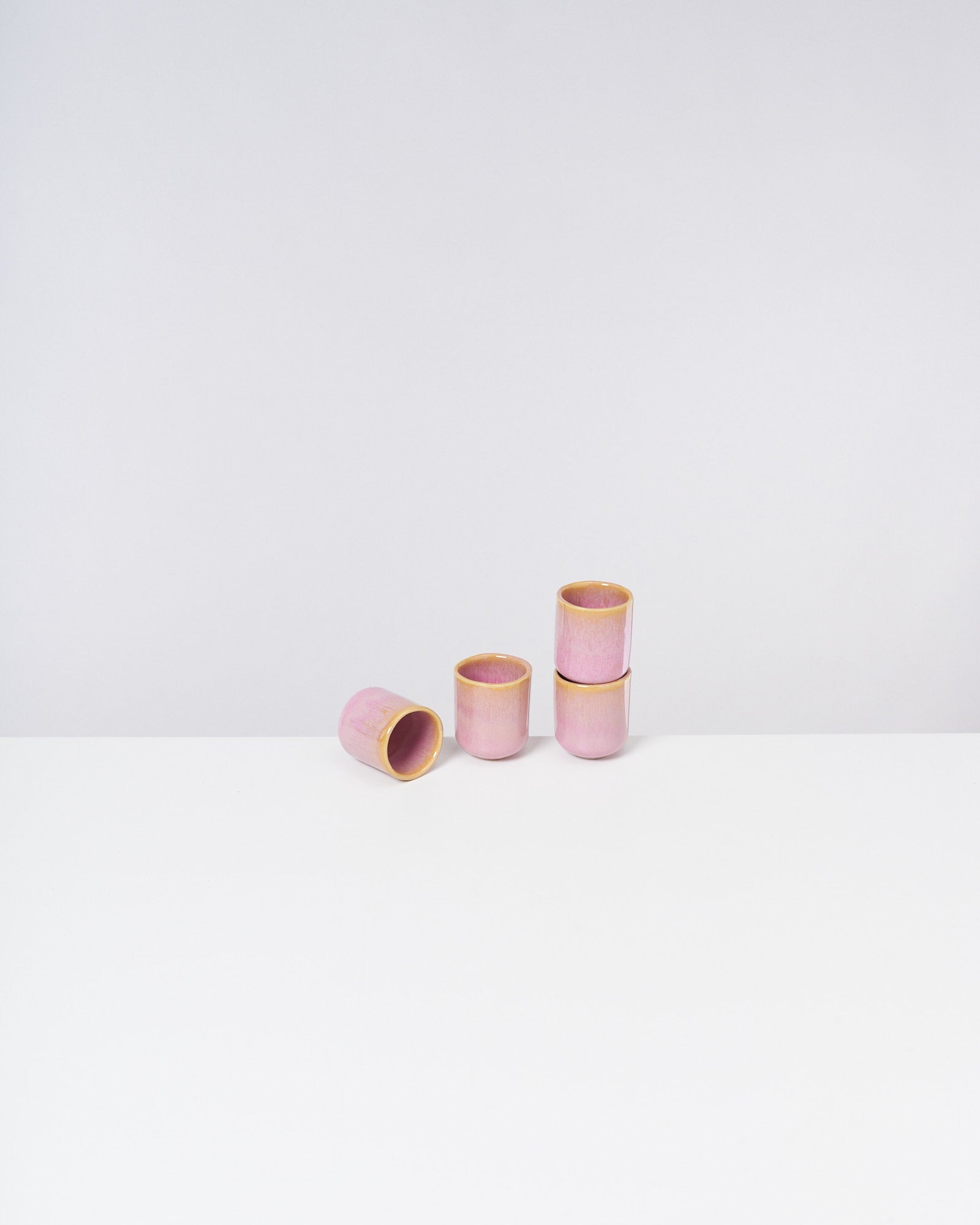Vier rosafarbene Tassen mit gelbem Rand, eine liegt seitlich, die anderen stehen aufrecht auf weißem Hintergrund.