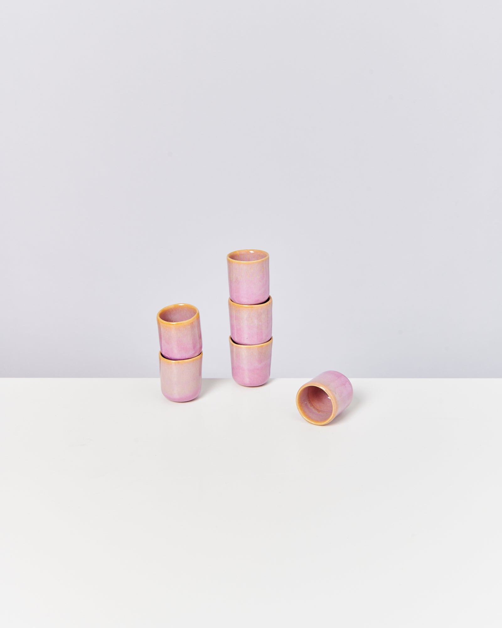 Drei Stapel kleiner, rosa Keramiktassen auf Tischfläche, jeweils zwei Tassen übereinander; eine liegt quer.