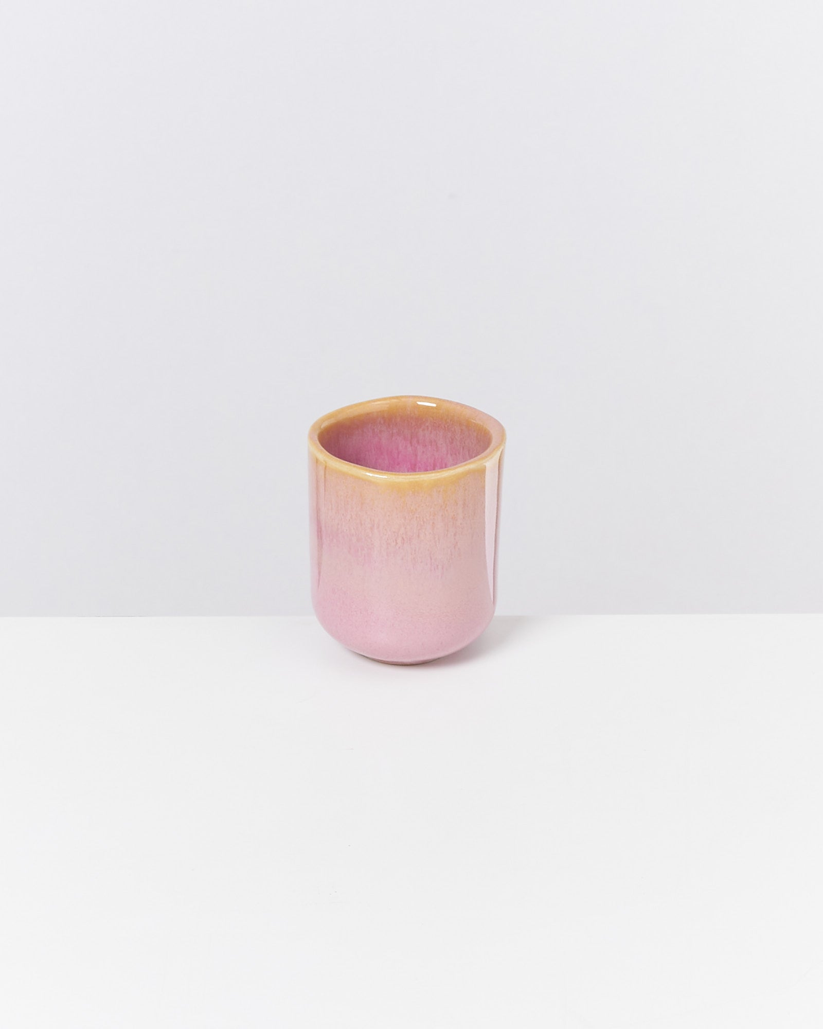 Rosa Keramikbecher mit gelbem Rand steht auf einer weißen Oberfläche vor einem weißen Hintergrund.