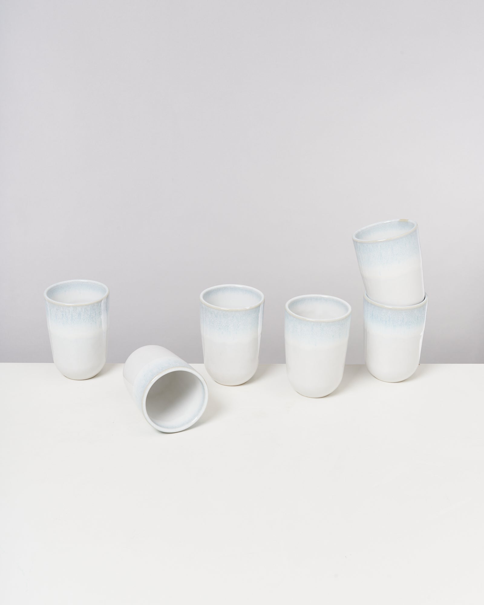 Sechs weiße Becher auf einem weißen Hintergrund, davon einer liegend und zwei übereinander gestapelt.