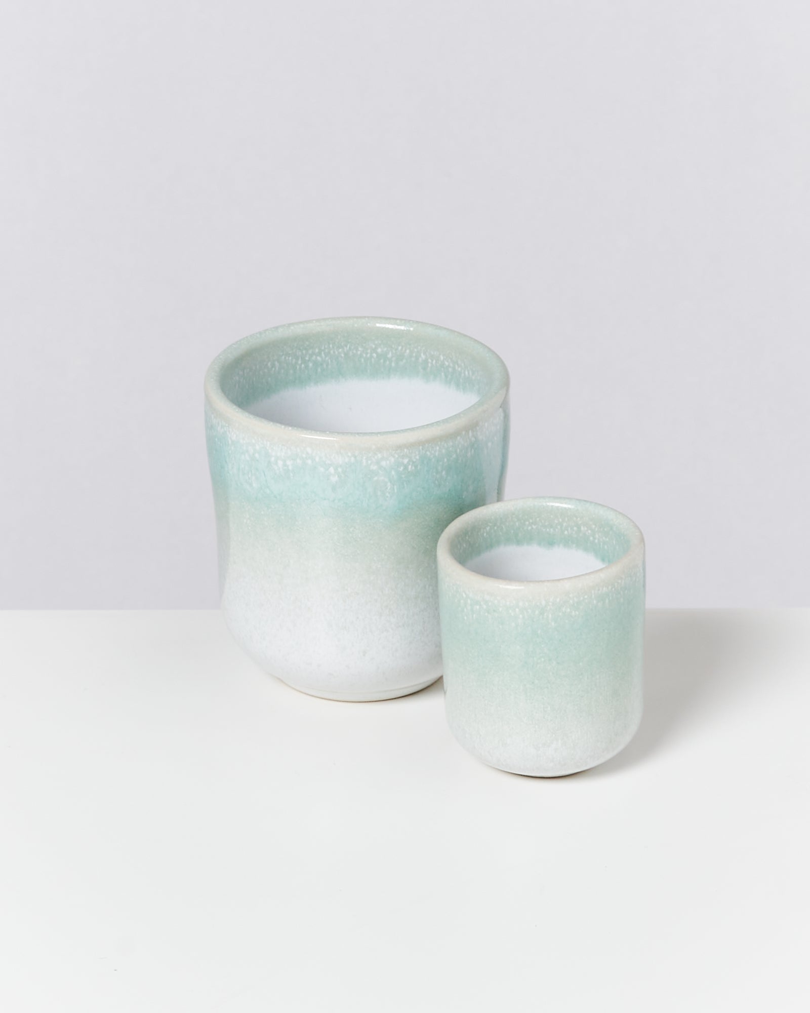 Zwei Keramiktöpfe in Grün und Weiß auf einer weißen Oberfläche, ein größerer und ein kleinerer.