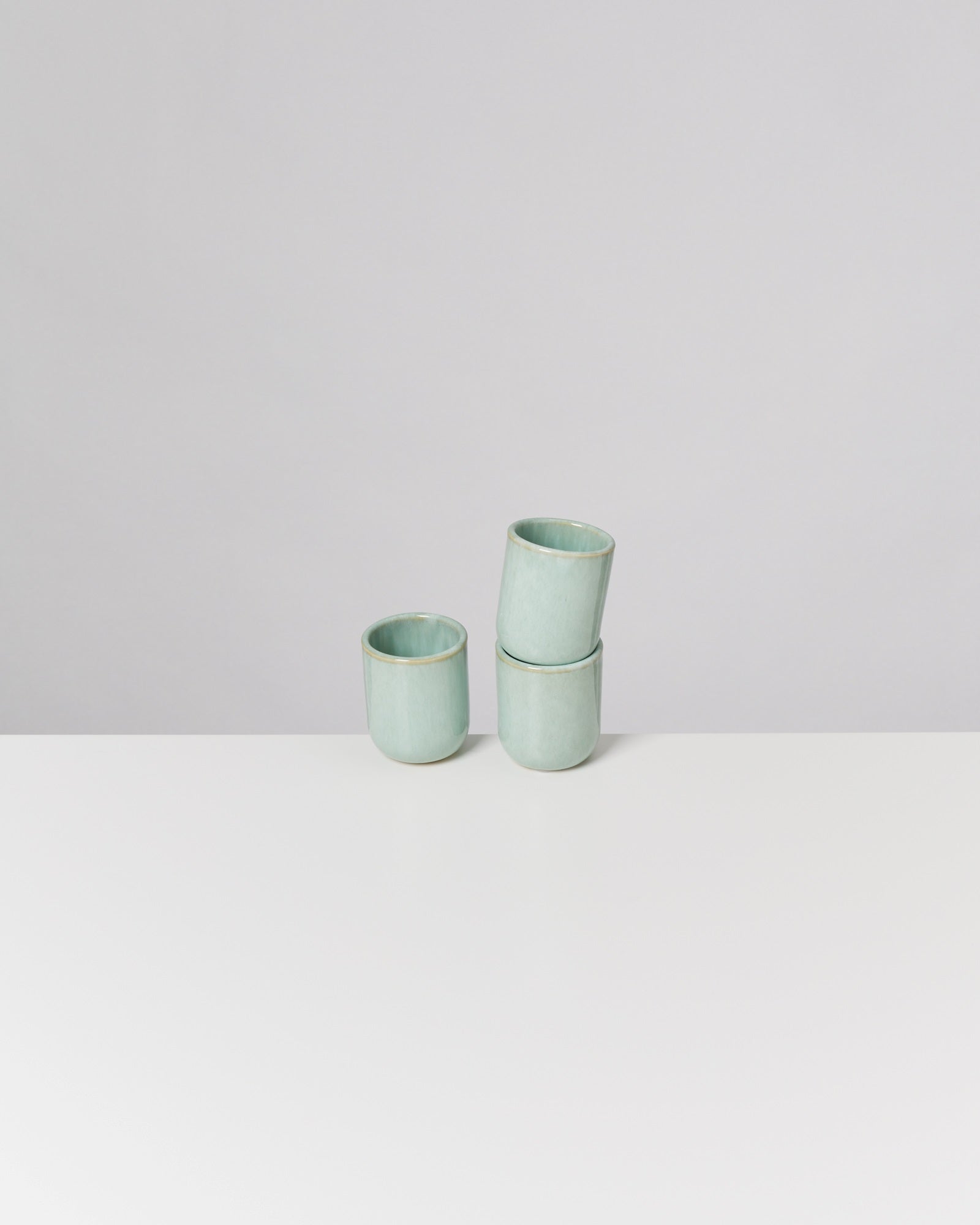 Drei türkisfarbene Keramikbecher auf einem weißen Tisch, zwei gestapelt und einer separat stehend.