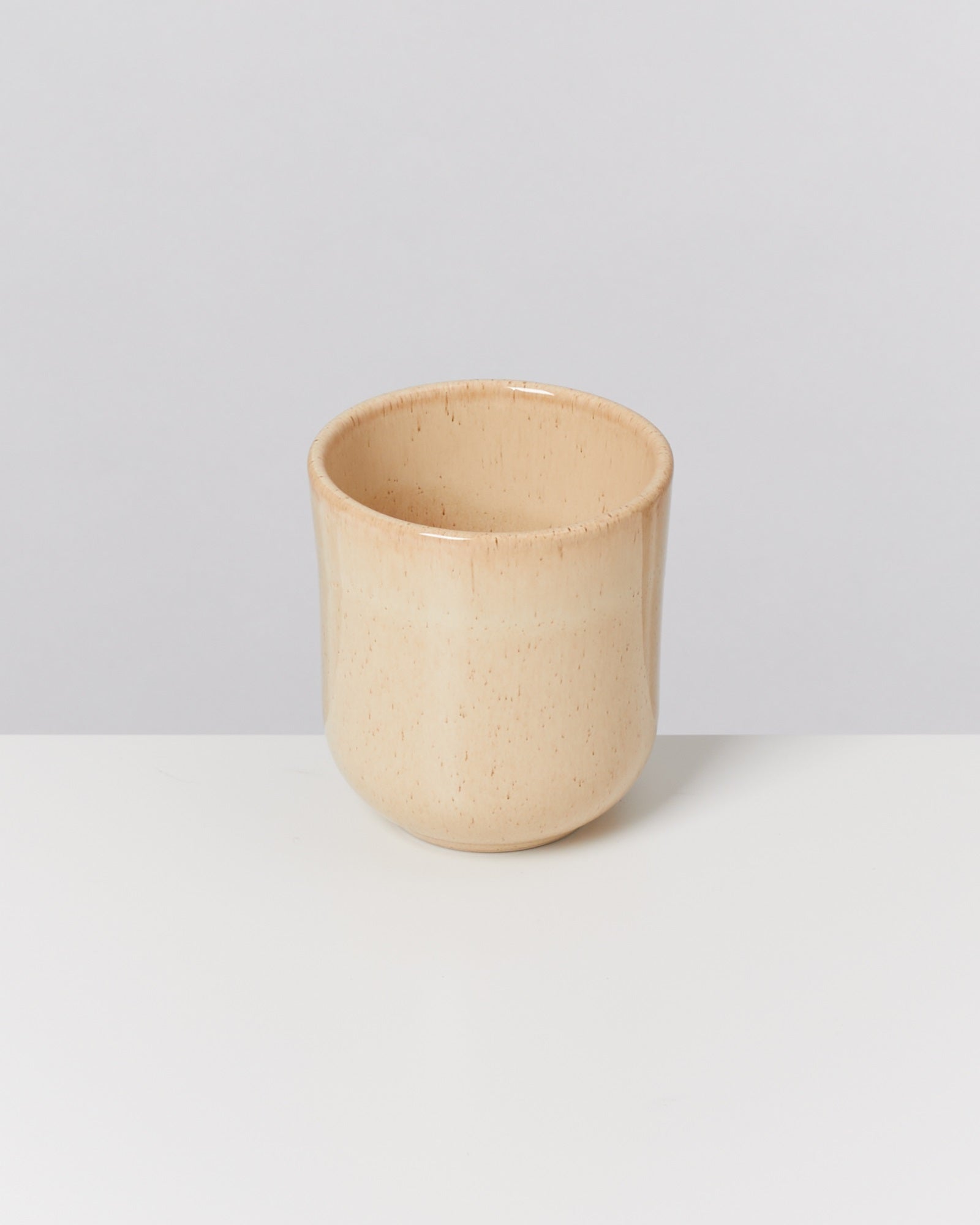 Beigefarbene Keramiktasse auf weißem Hintergrund.