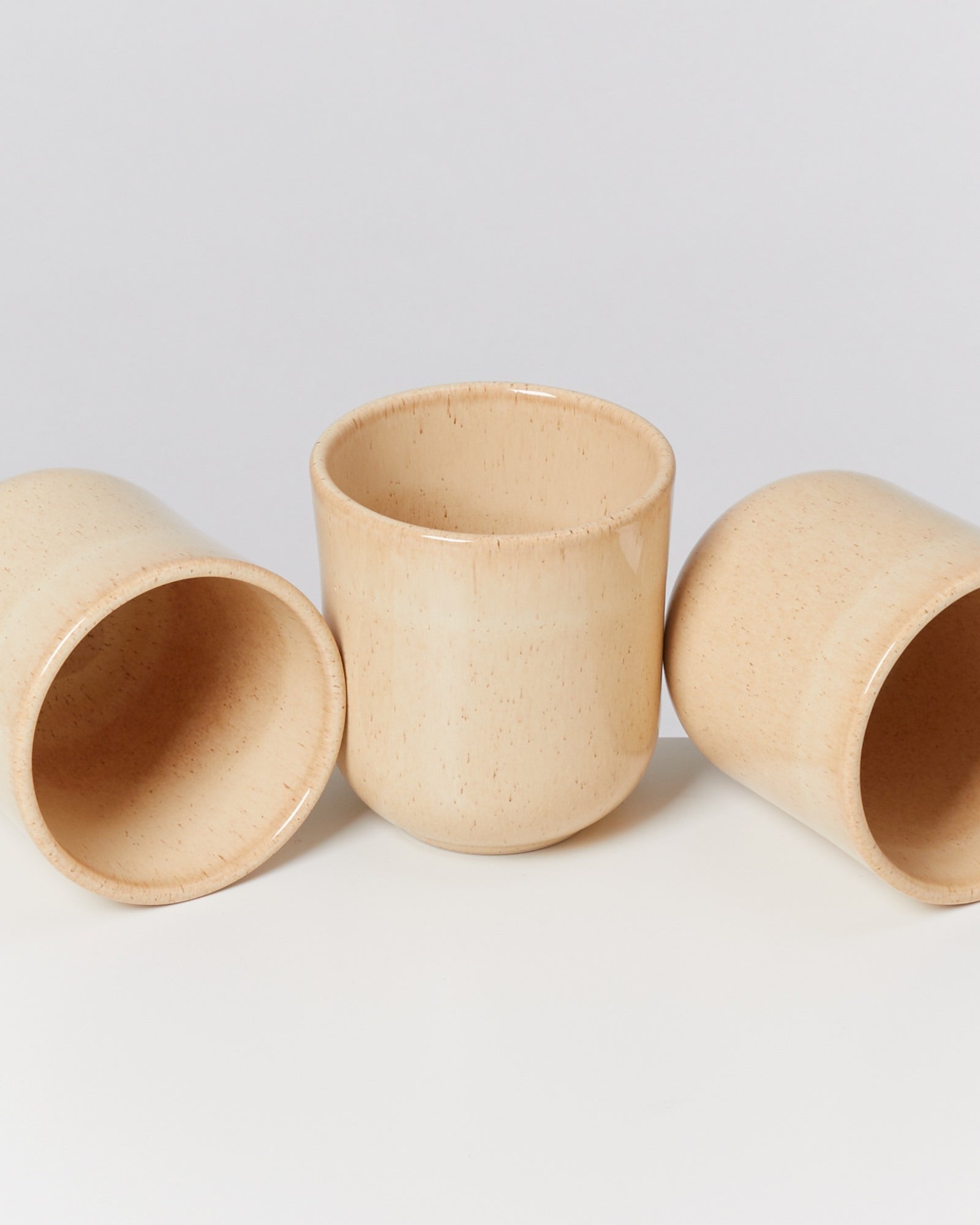 Drei beige Keramiktassen, zwei liegend und eine stehend, vor einem weißen Hintergrund.