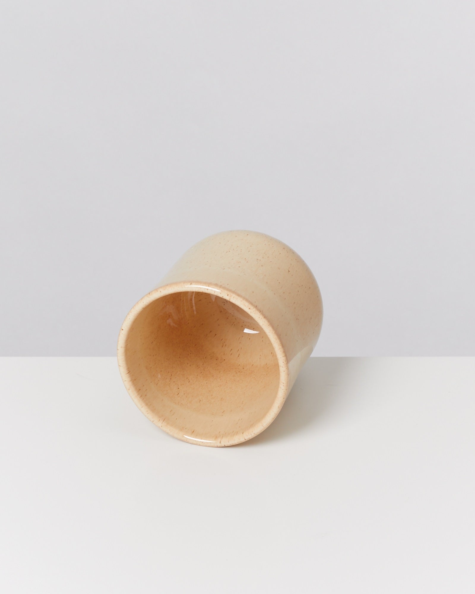 Beiger Keramikbecher, seitlich liegend auf weißem Hintergrund.