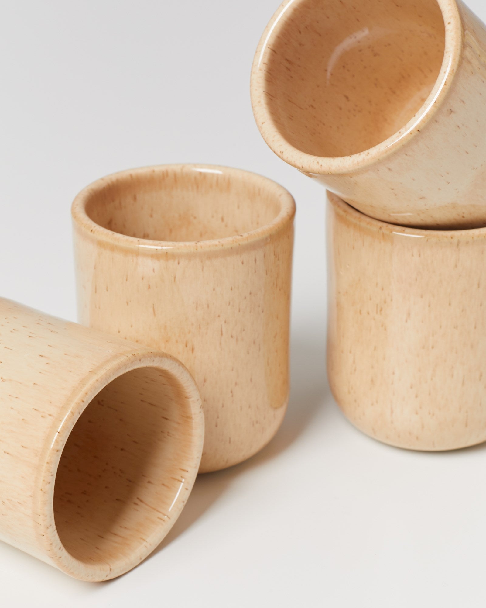 Vier beigefarbene Keramikbecher stapeln sich auf einer weißen Oberfläche.