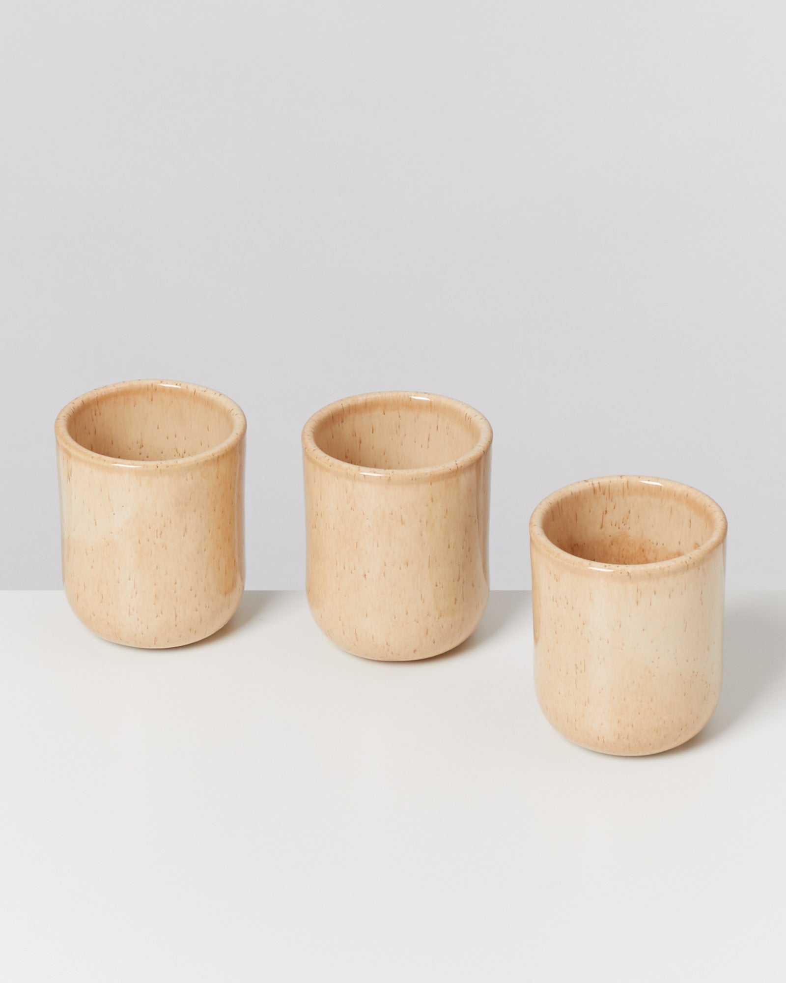 Drei beigefarbene Keramikbecher stehen in einer Reihe auf einer weißen Oberfläche.