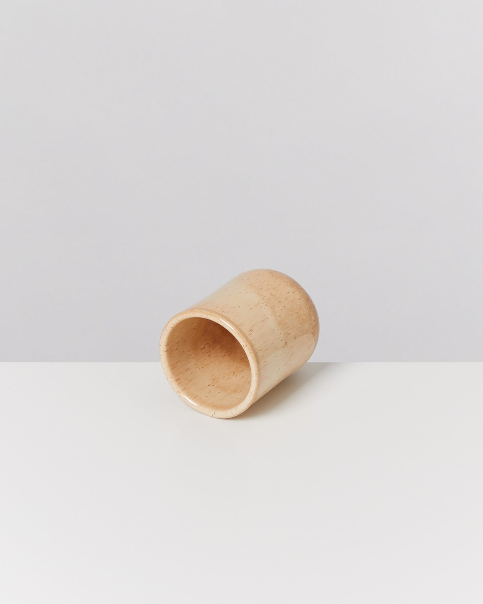 Holzbecher liegt seitlich auf einem weißen Tisch vor einem neutralen Hintergrund.