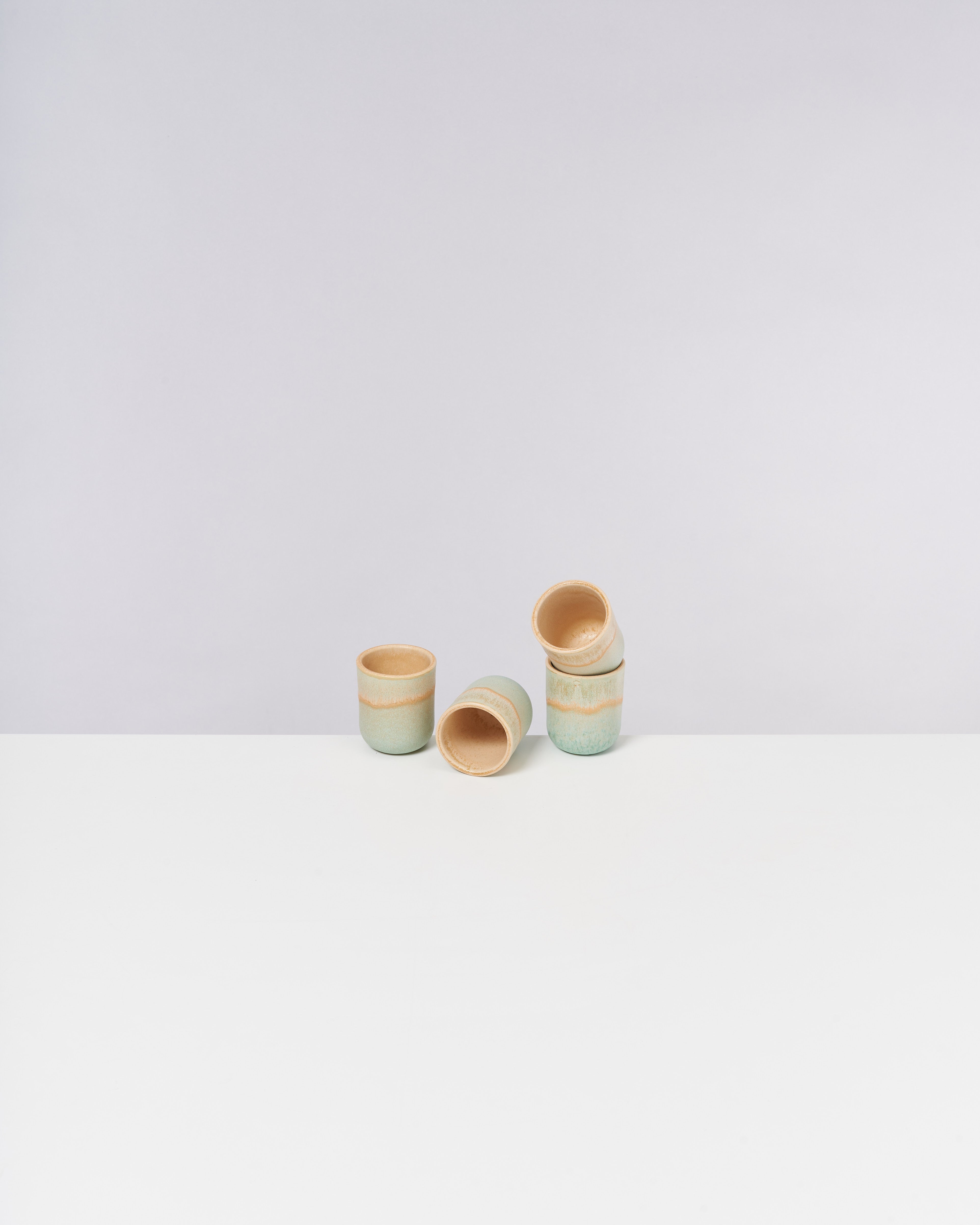 Fünf übereinander gestapelte Keramikbecher auf einem weißen Tisch vor grauem Hintergrund.
