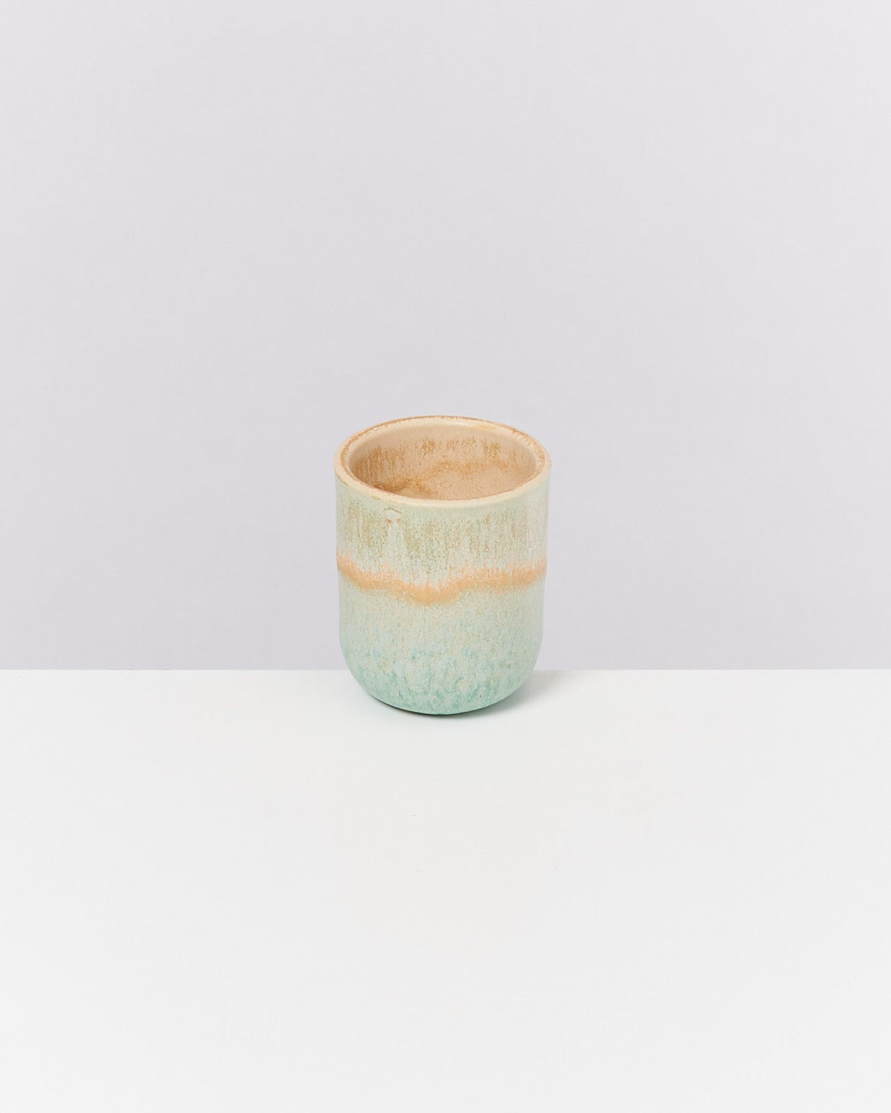 Keramikbecher mit grün-beige Muster auf weißem Hintergrund.