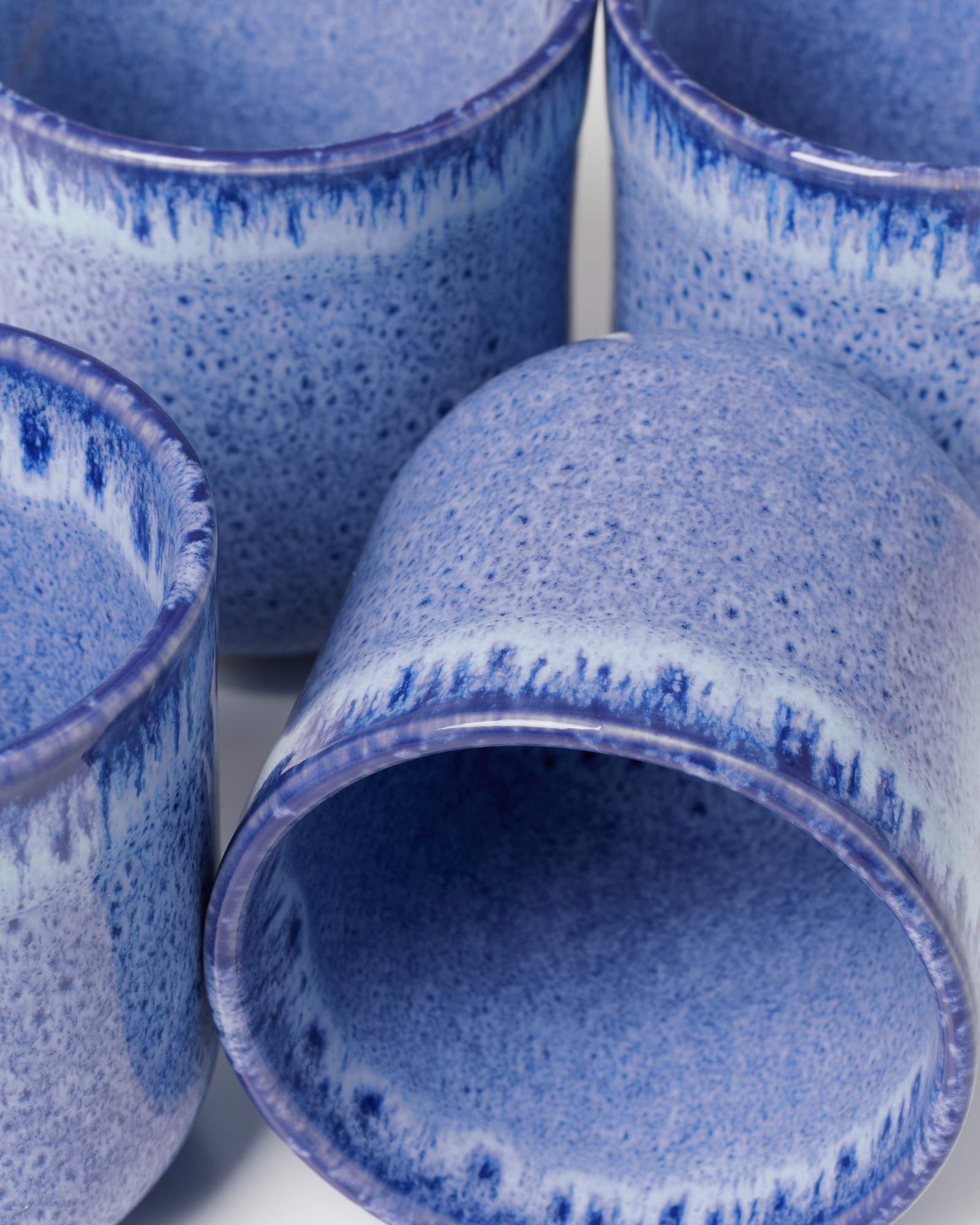 Fünf blaue Keramiktassen mit gesprenkeltem Muster auf weißem Hintergrund, eine liegt seitlich.
