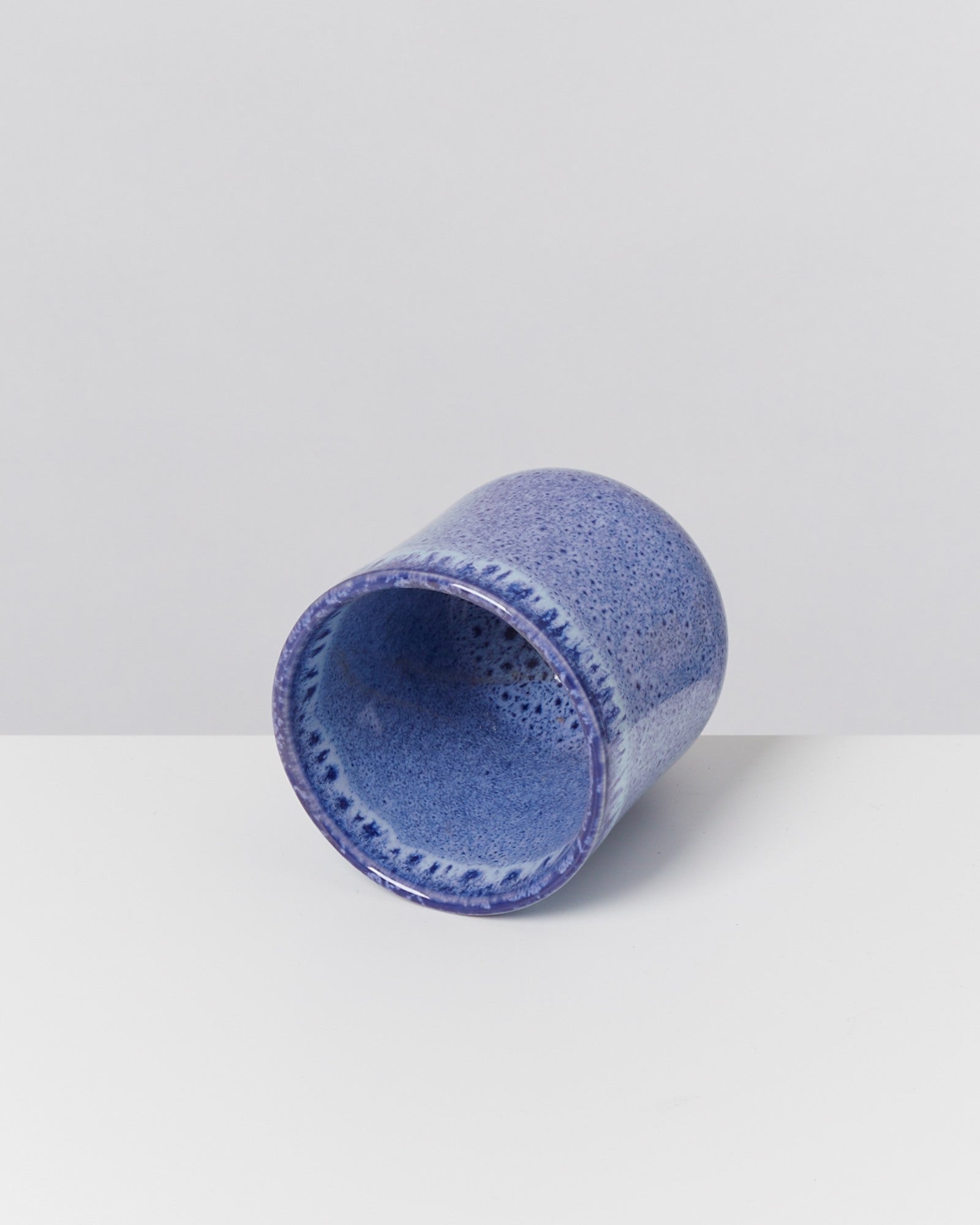 Blauer, keramischer Becher liegt auf der Seite auf einer weißen Oberfläche.