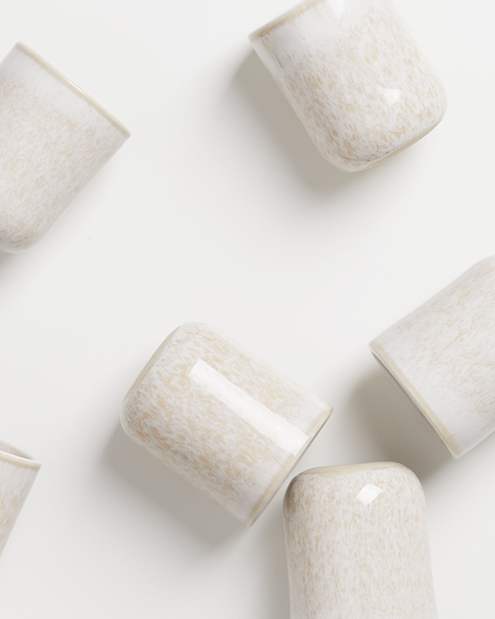 Mehrere cremefarbene Keramiktassen liegen unregelmäßig auf einer weißen Oberfläche.