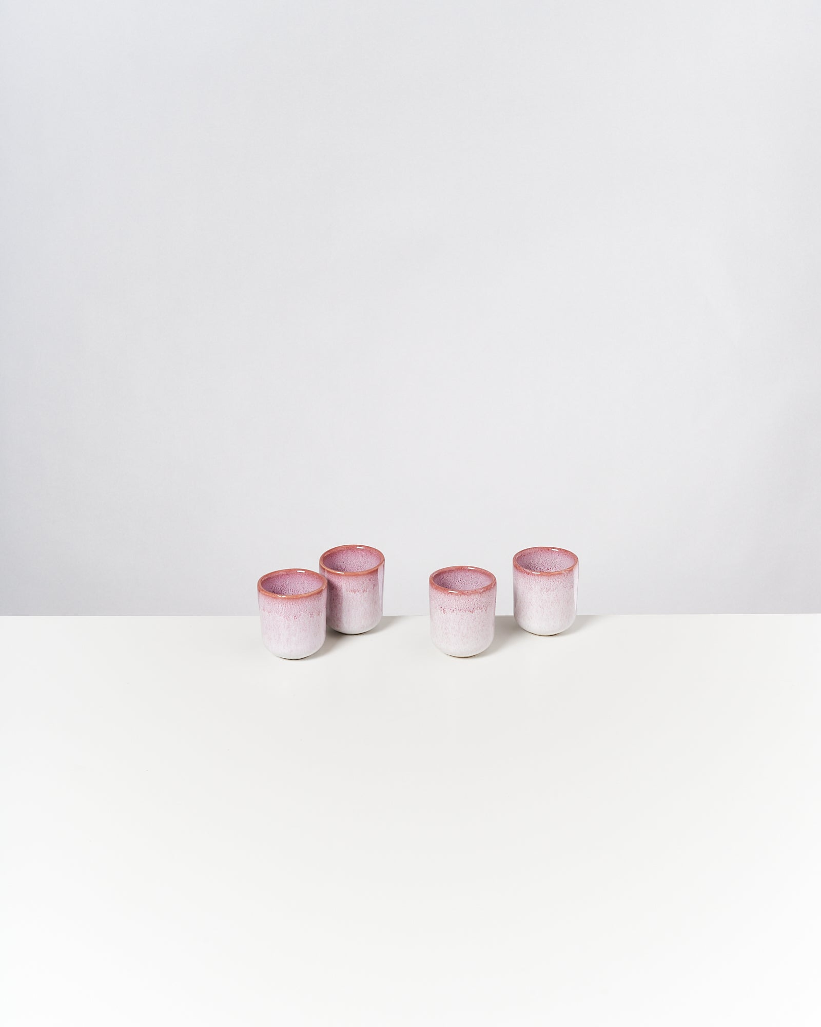 Vier kleine rosa-weiße Töpfe stehen auf einem weißen Tisch vor einem grauen Hintergrund.