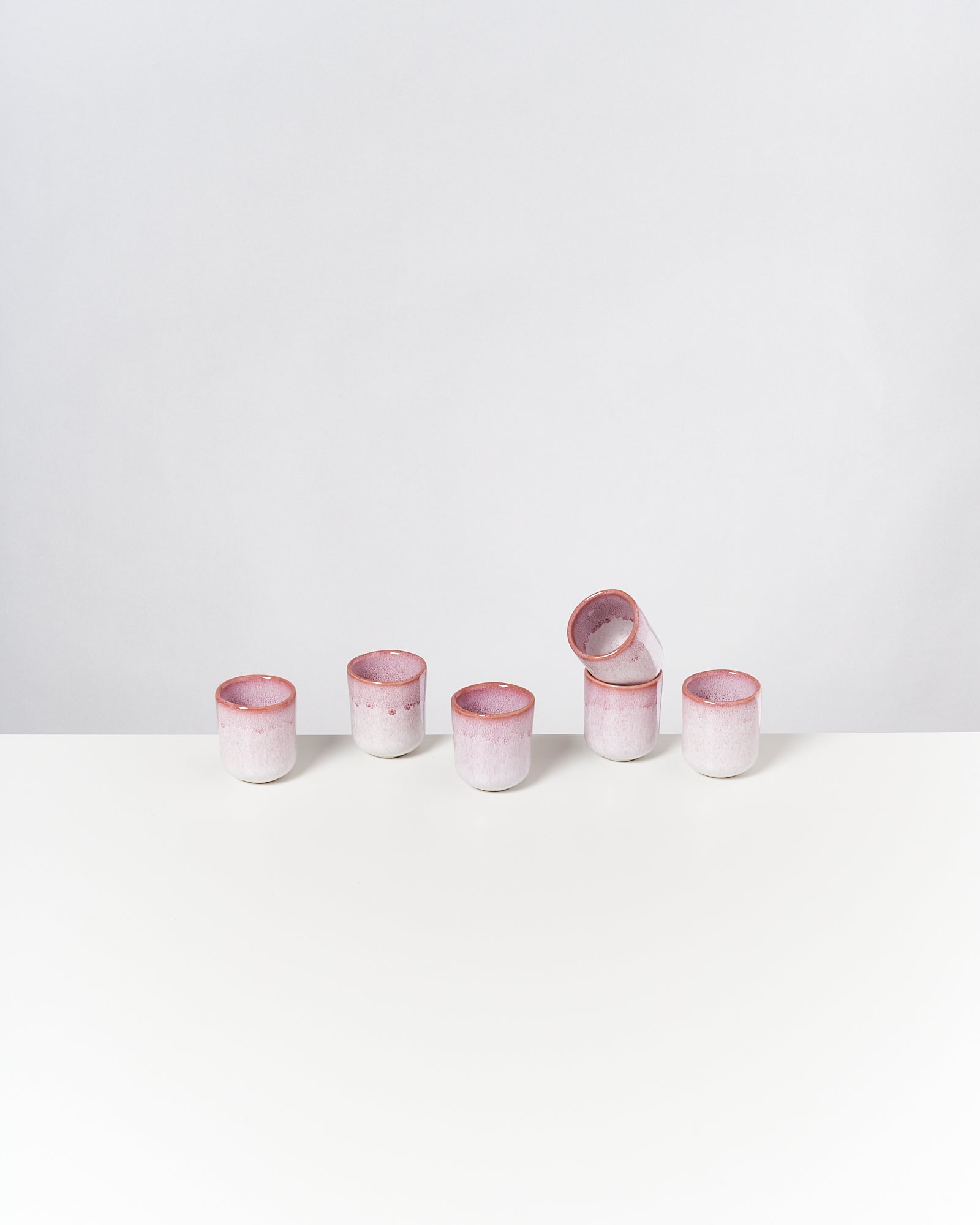 Fünf rosa Keramikbecher auf einem weißen Tisch, einer liegt auf der Seite.