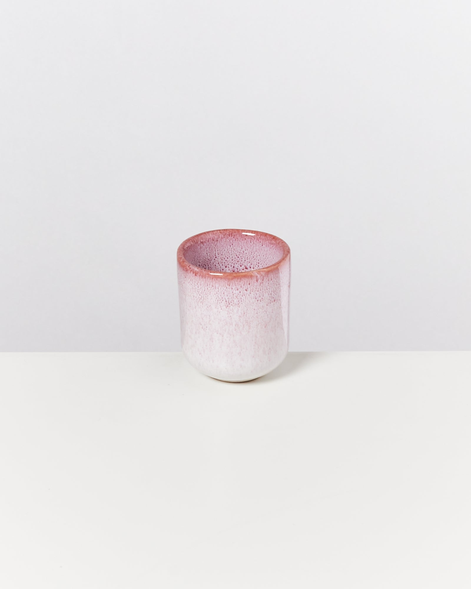 Keramikbecher mit verlaufender rosa-weißer Glasur auf weißem Hintergrund.