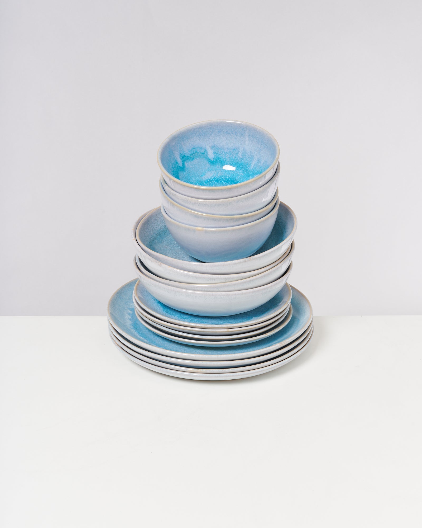 Ein Stapel aus blauen und grauen Keramikschalen und Tellern auf weißem Hintergrund.