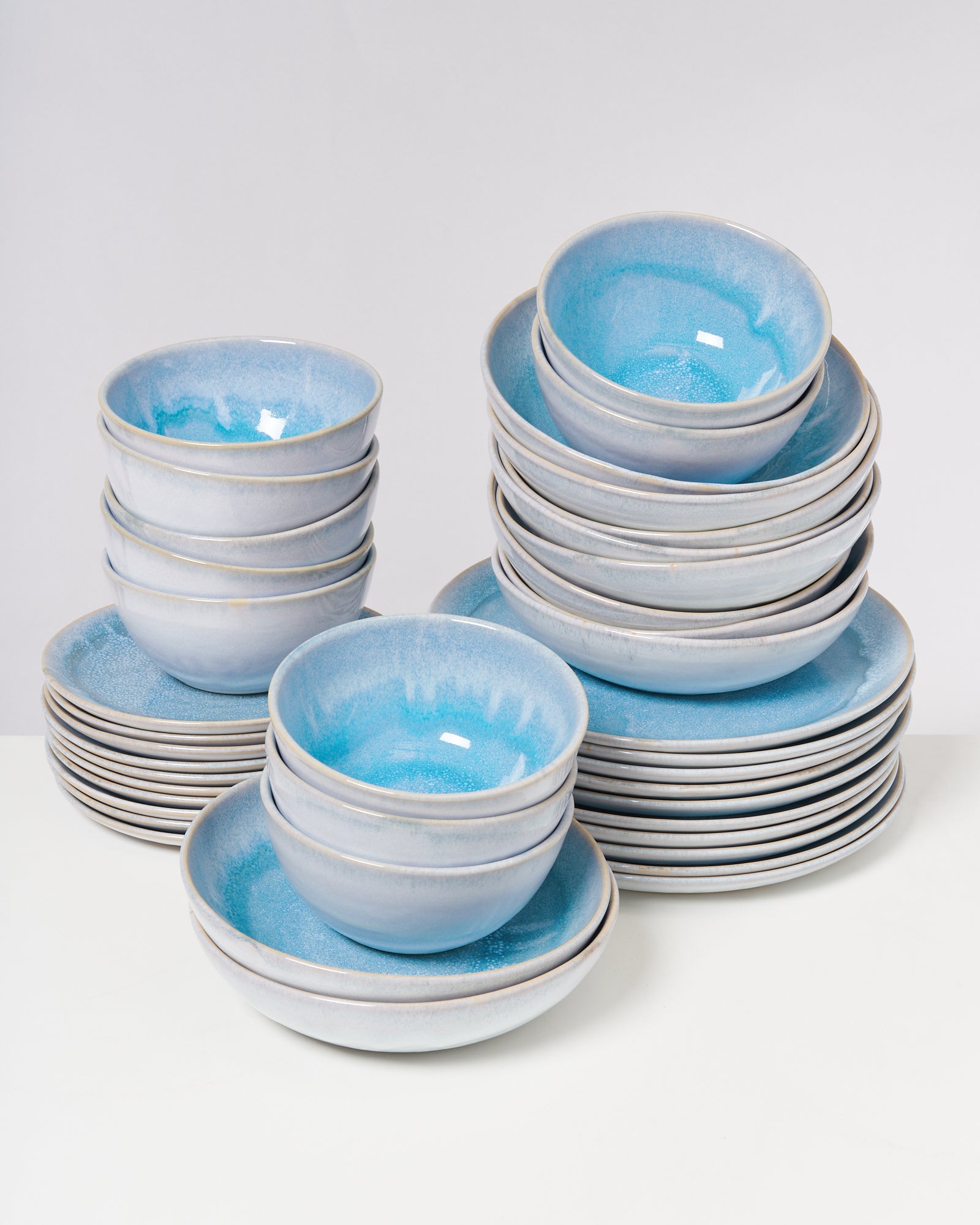 Gestapelte blaue Keramikschalen und -teller mit glänzender Glasur auf einem weißen Hintergrund.