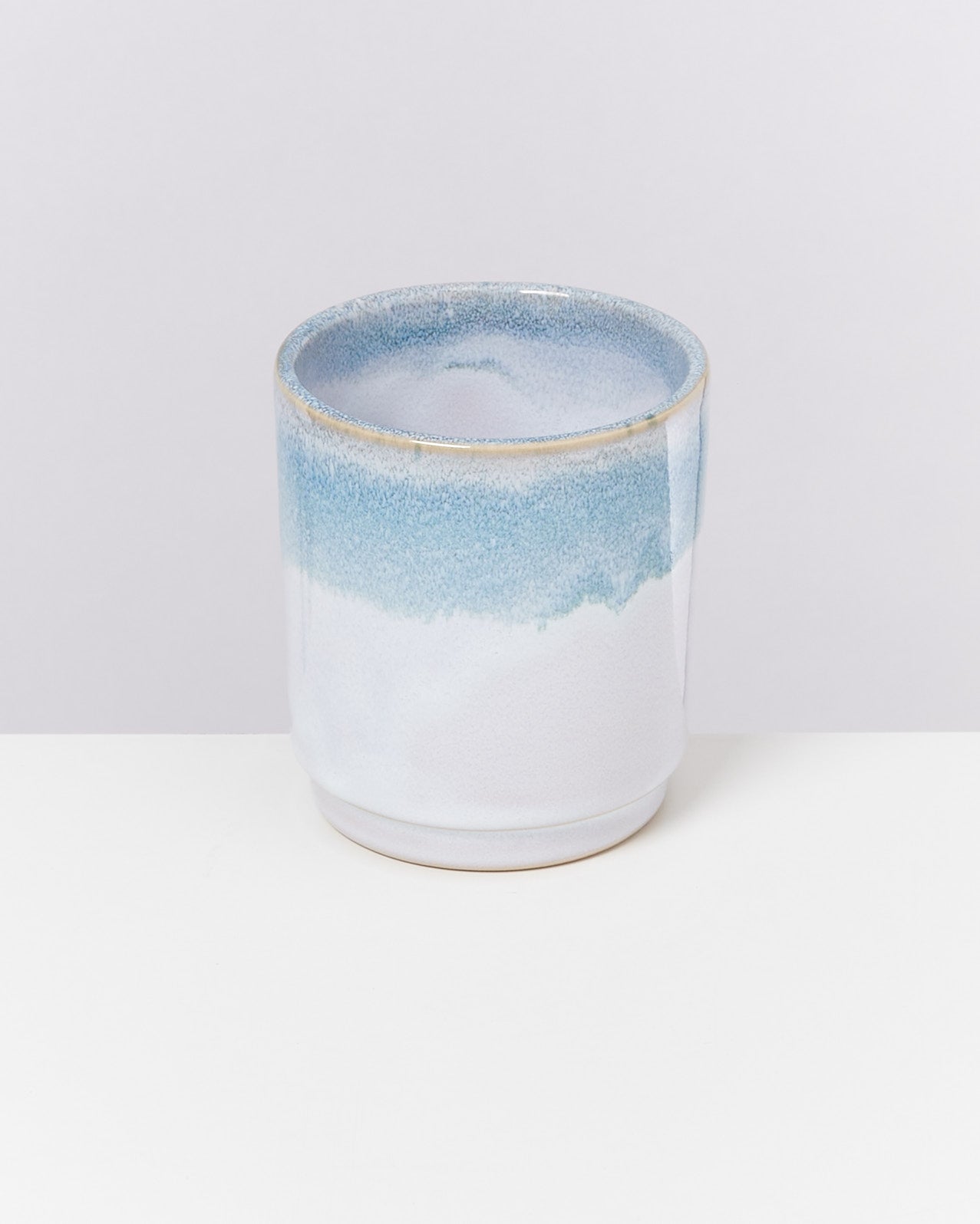 Keramikbecher mit blauem Farbverlauf, auf einem weißen Hintergrund stehend.