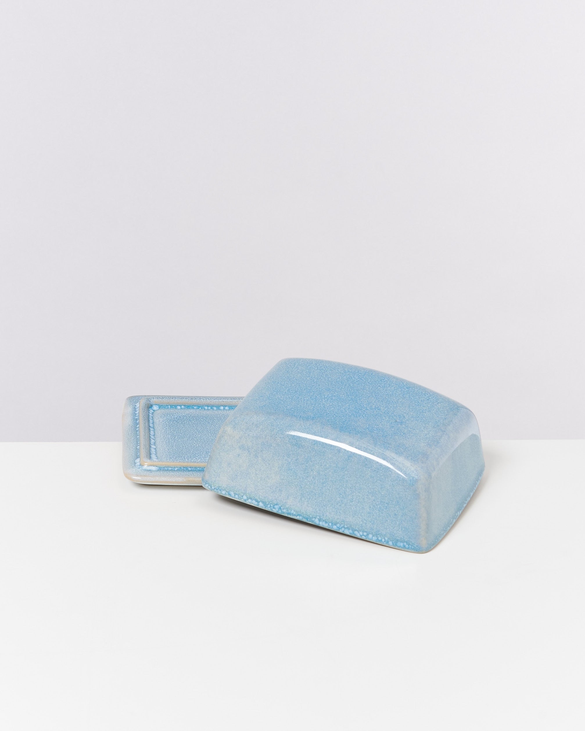 Blaue Keramikbutterdose auf weißem Hintergrund, bestehend aus einem Deckel und einer flachen Unterlage.