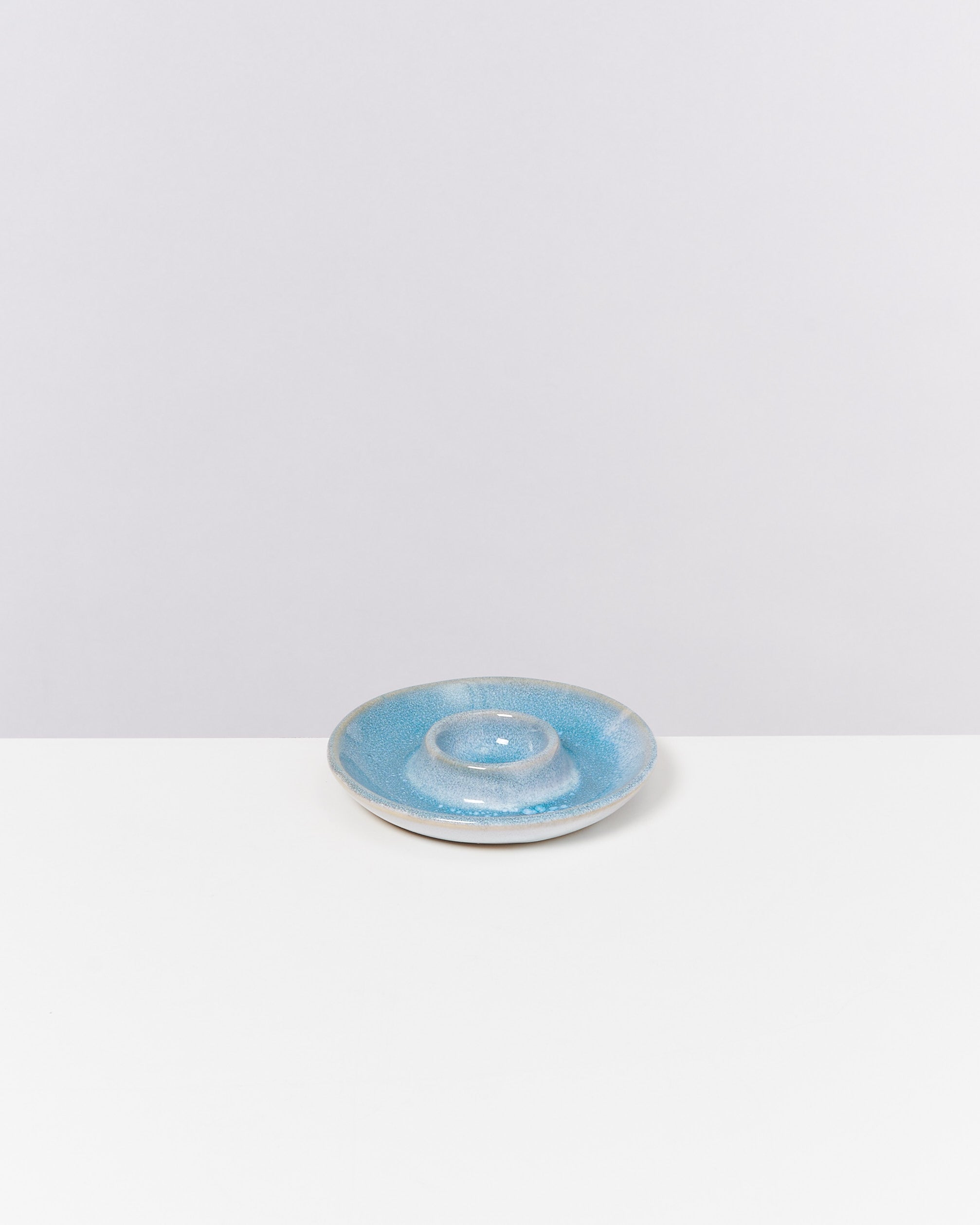 Kleiner, hellblauer Keramikteller mit erhöhtem Rand auf weißem Hintergrund.