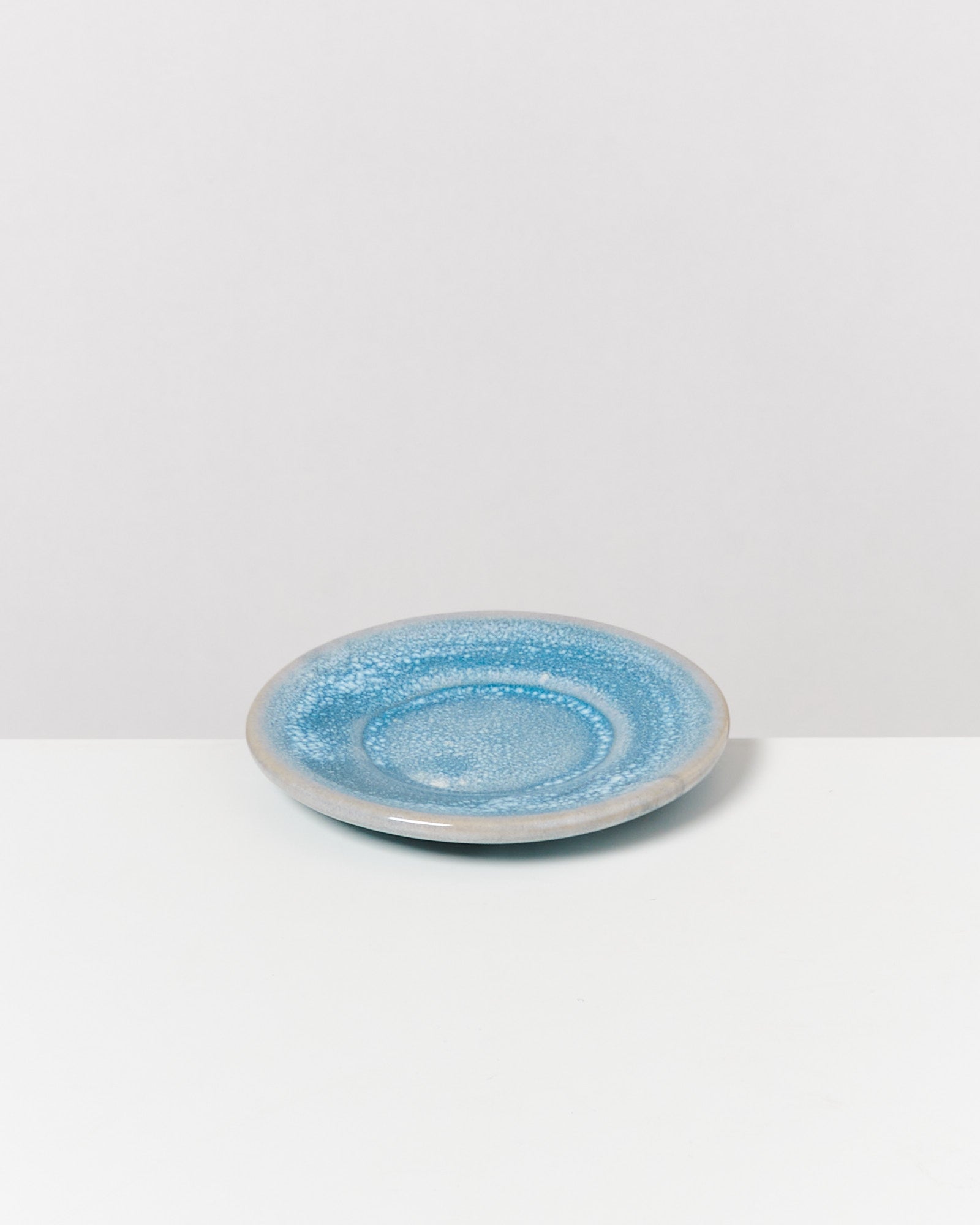 Blauer, flacher Keramikteller mit gesprenkelter Glasur auf weißem Hintergrund.