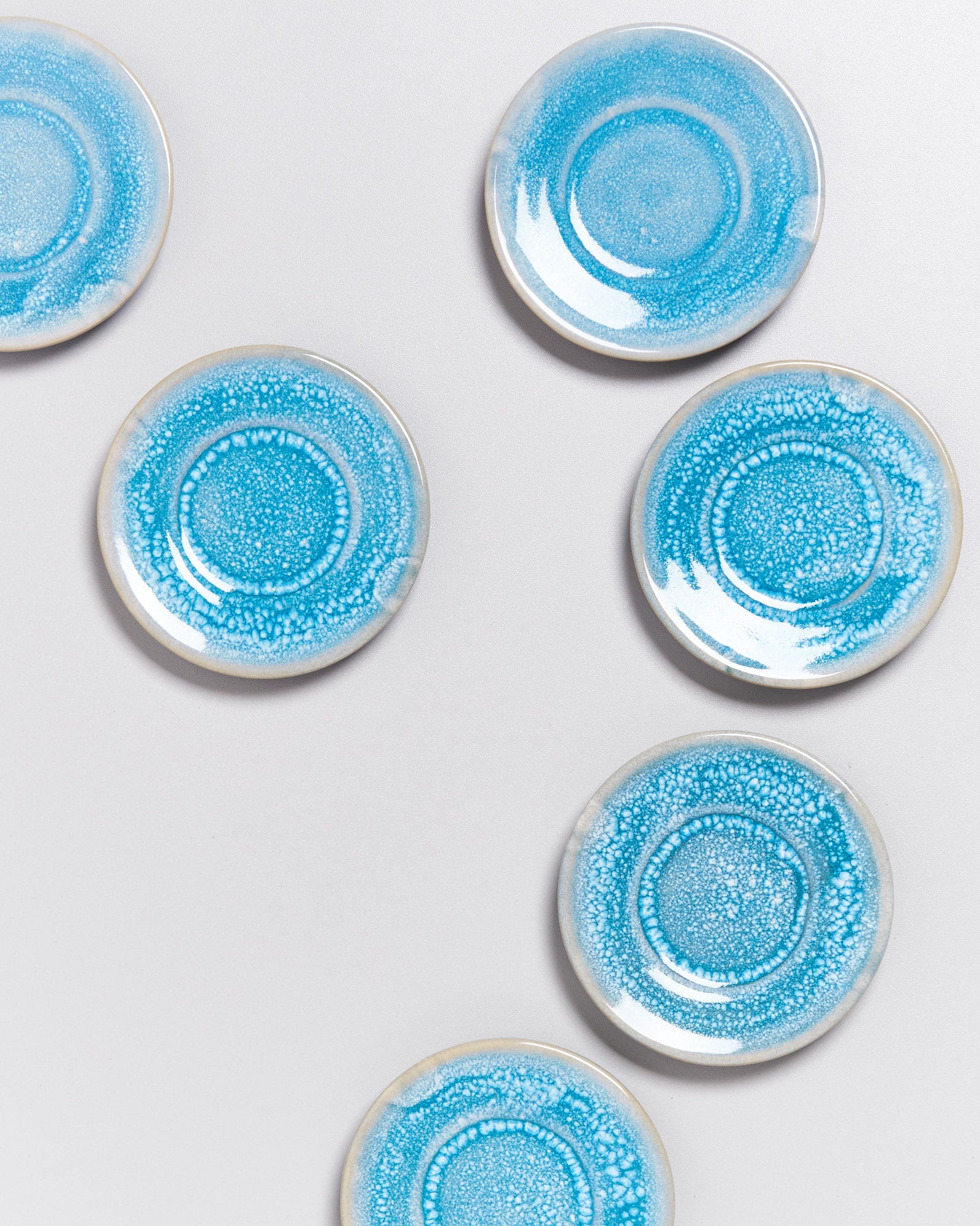 Sechs blaue, marmorierte Untertassen sind auf einer weißen Fläche kreisförmig angeordnet.