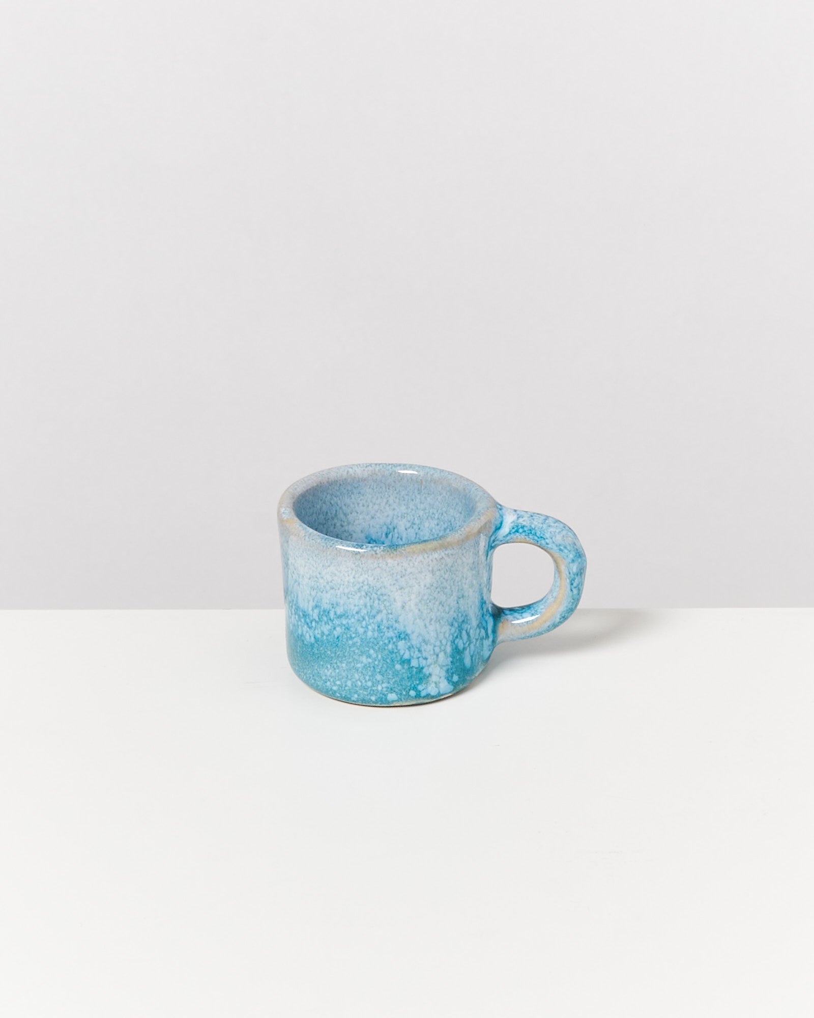 Eine kleine, blaue Keramiktasse mit Henkel steht auf einem weißen Hintergrund.