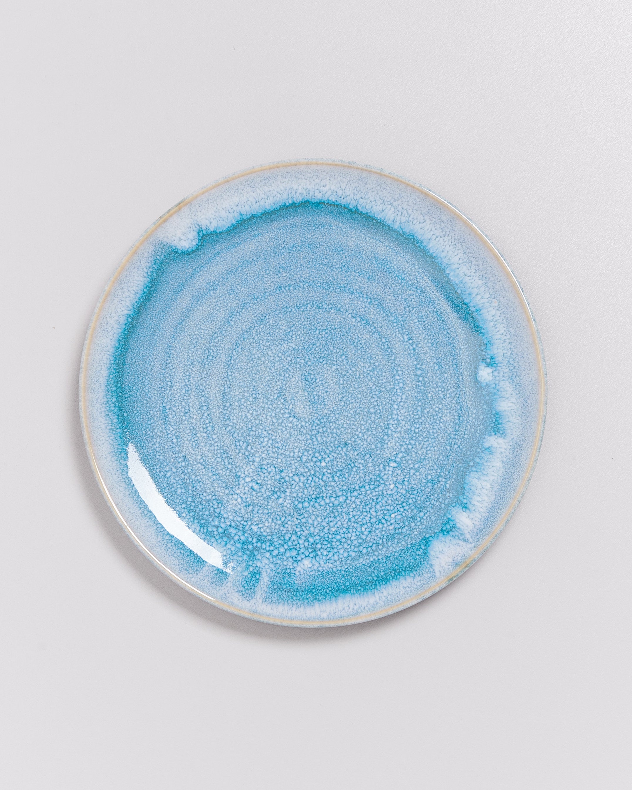 Runder Teller mit blauer, marmorierter Glasur auf einem weißen Hintergrund.