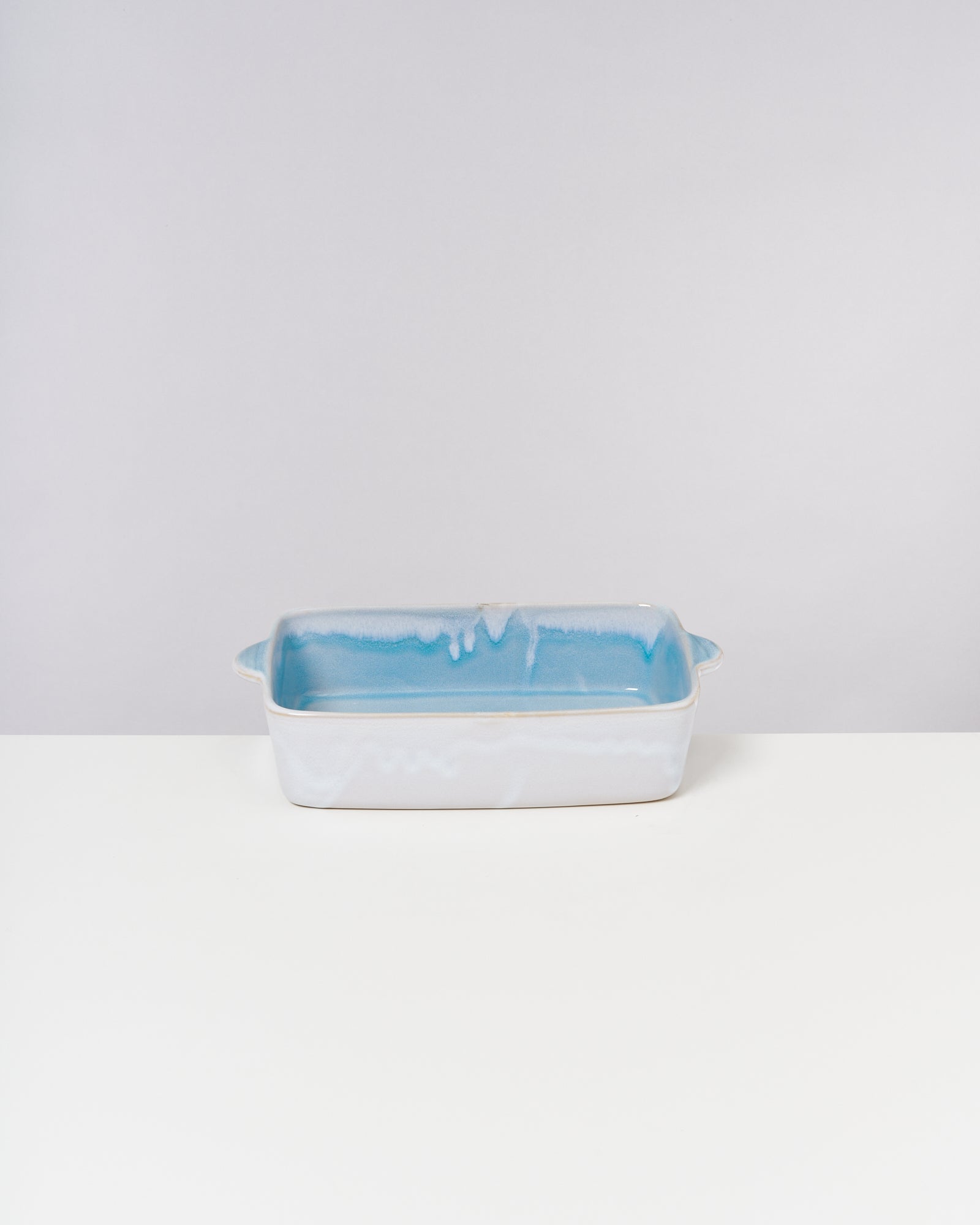 Rechteckige, blau-weiße Keramikbackform mit Henkeln steht auf einer weißen Oberfläche.