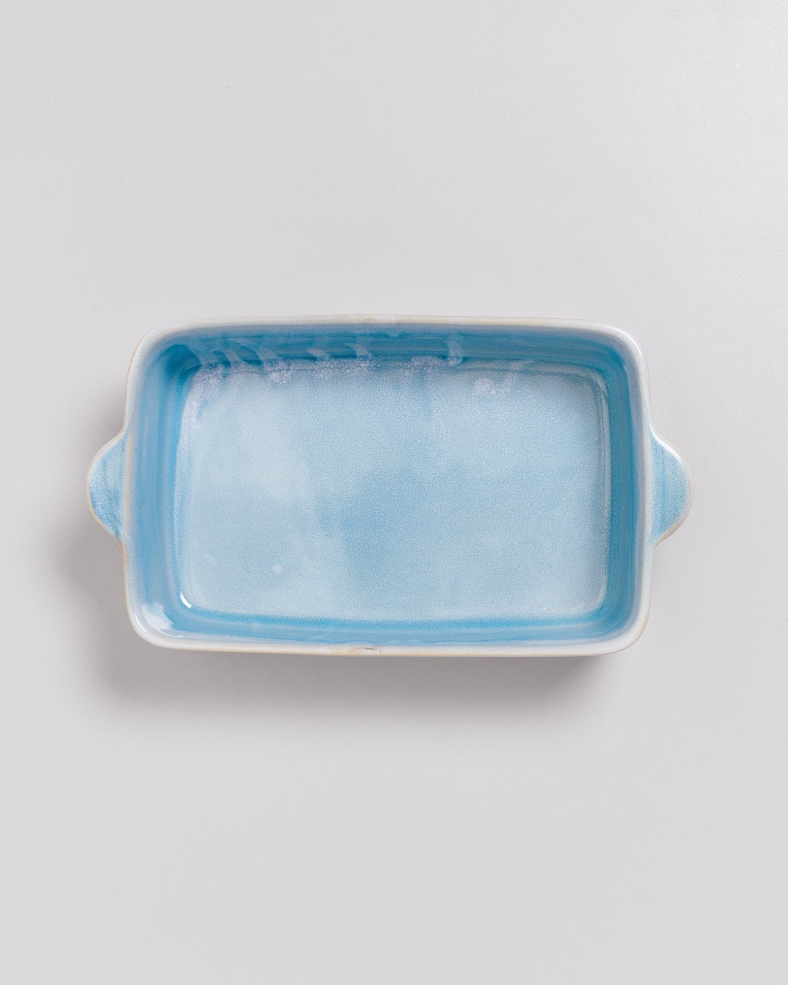 Rechteckige, hellblau glasierte Keramikauflaufform mit zwei Henkeln auf einem weißen Hintergrund.