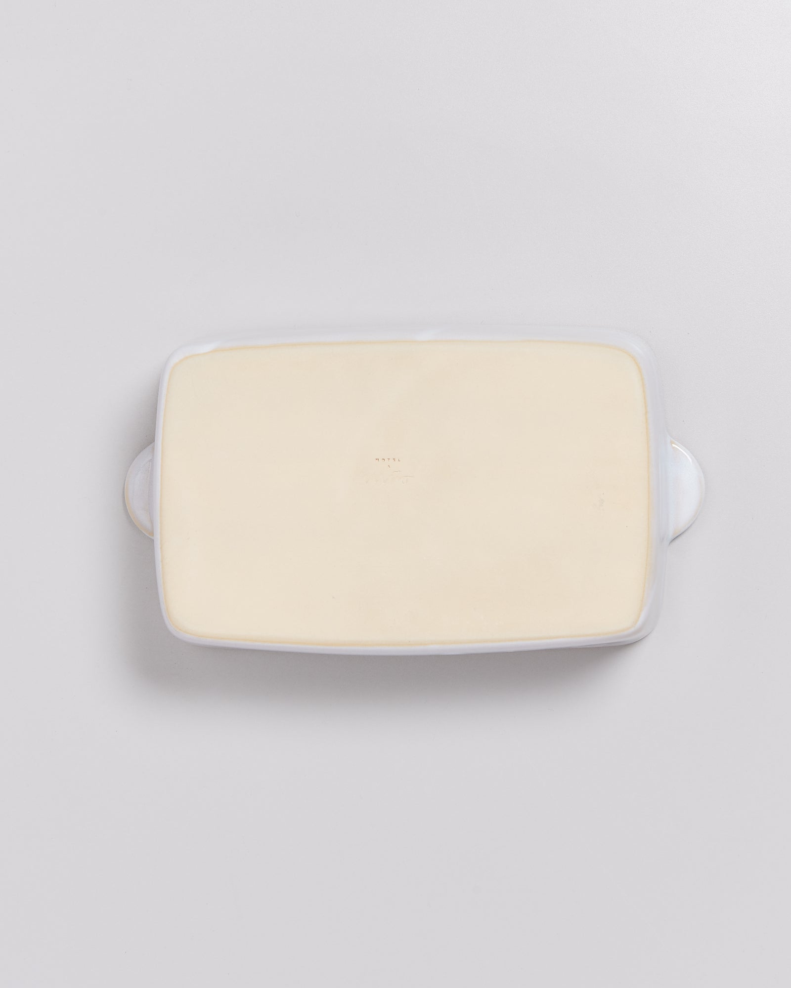 Rechteckige, weiße Butterdose mit hellem Inhalt, von oben auf einer hellgrauen Oberfläche fotografiert.