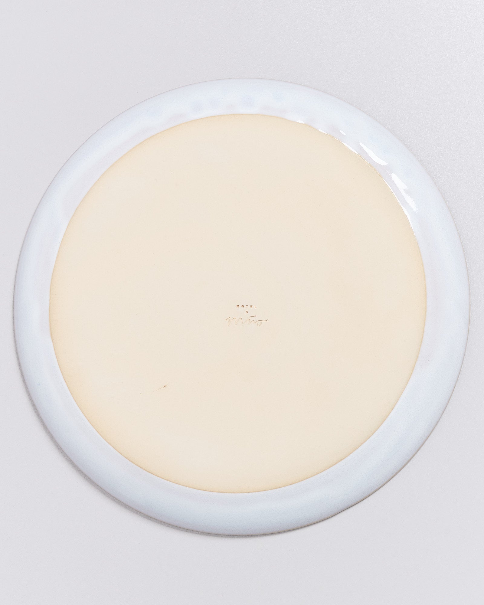 Rückseite eines Tellers mit heller Glasur und handschriftlicher Signatur in der Mitte auf cremefarbenem Hintergrund.