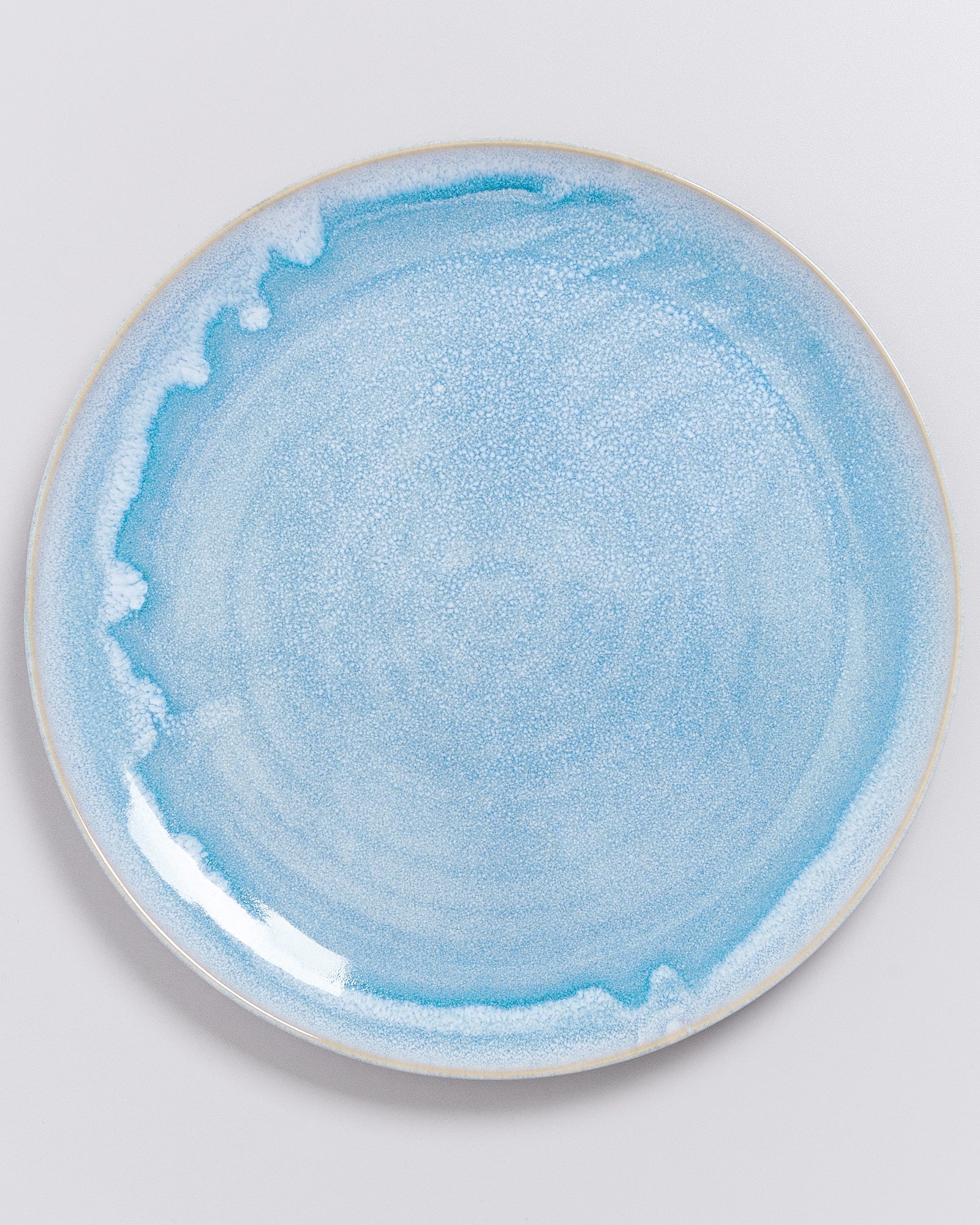 Runder Teller mit blau-weißer Glasur und wellenförmigem Muster auf weißem Hintergrund.