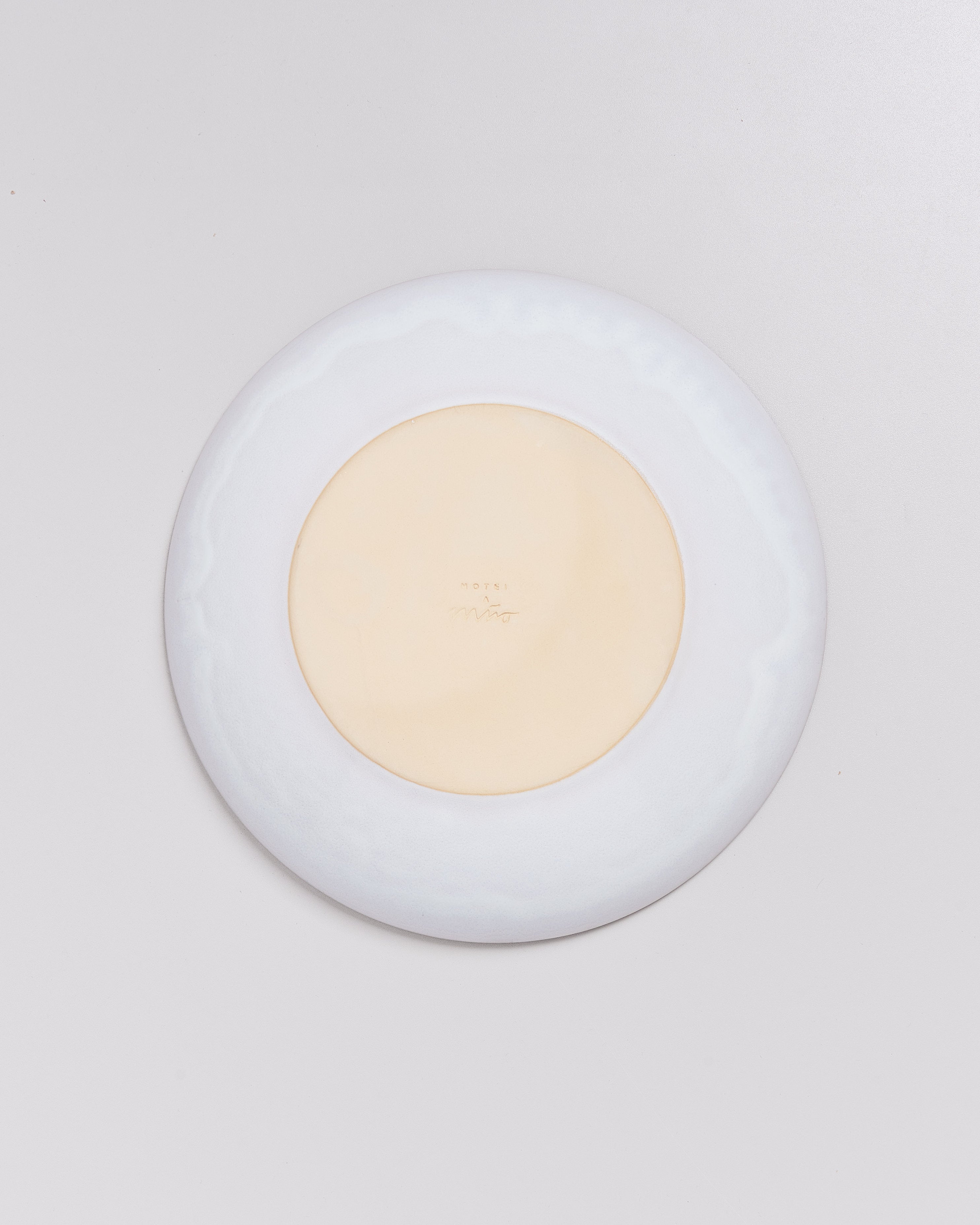 Rückseite eines weißen Tellers mit einem kreisförmigen, beigen Zentrum und eingraviertem Text.