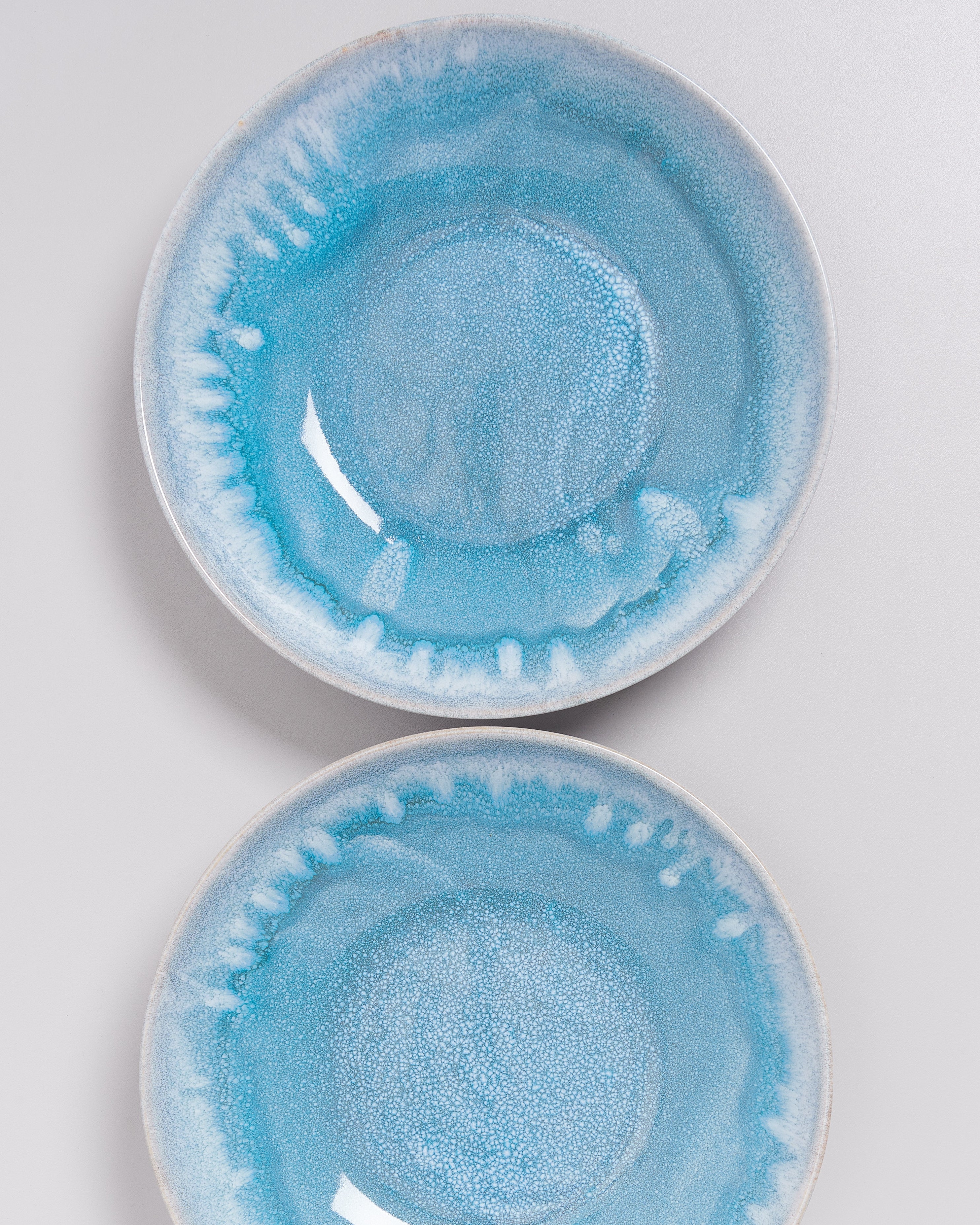Zwei blaue Teller mit weißem Randmuster liegen übereinander auf einer grauen Oberfläche.