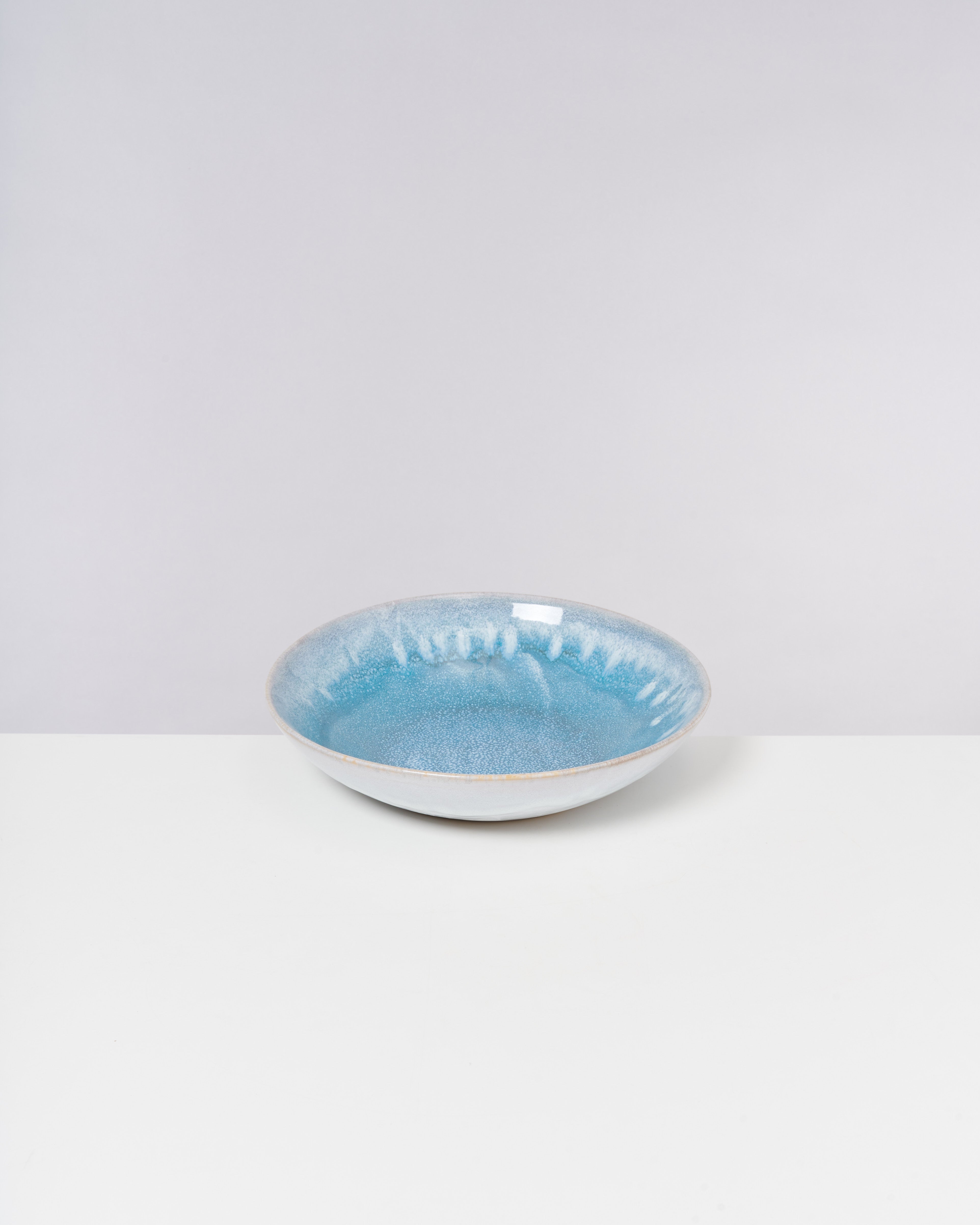 Eine flache, blaue Keramikschale auf einem weißen Hintergrund.