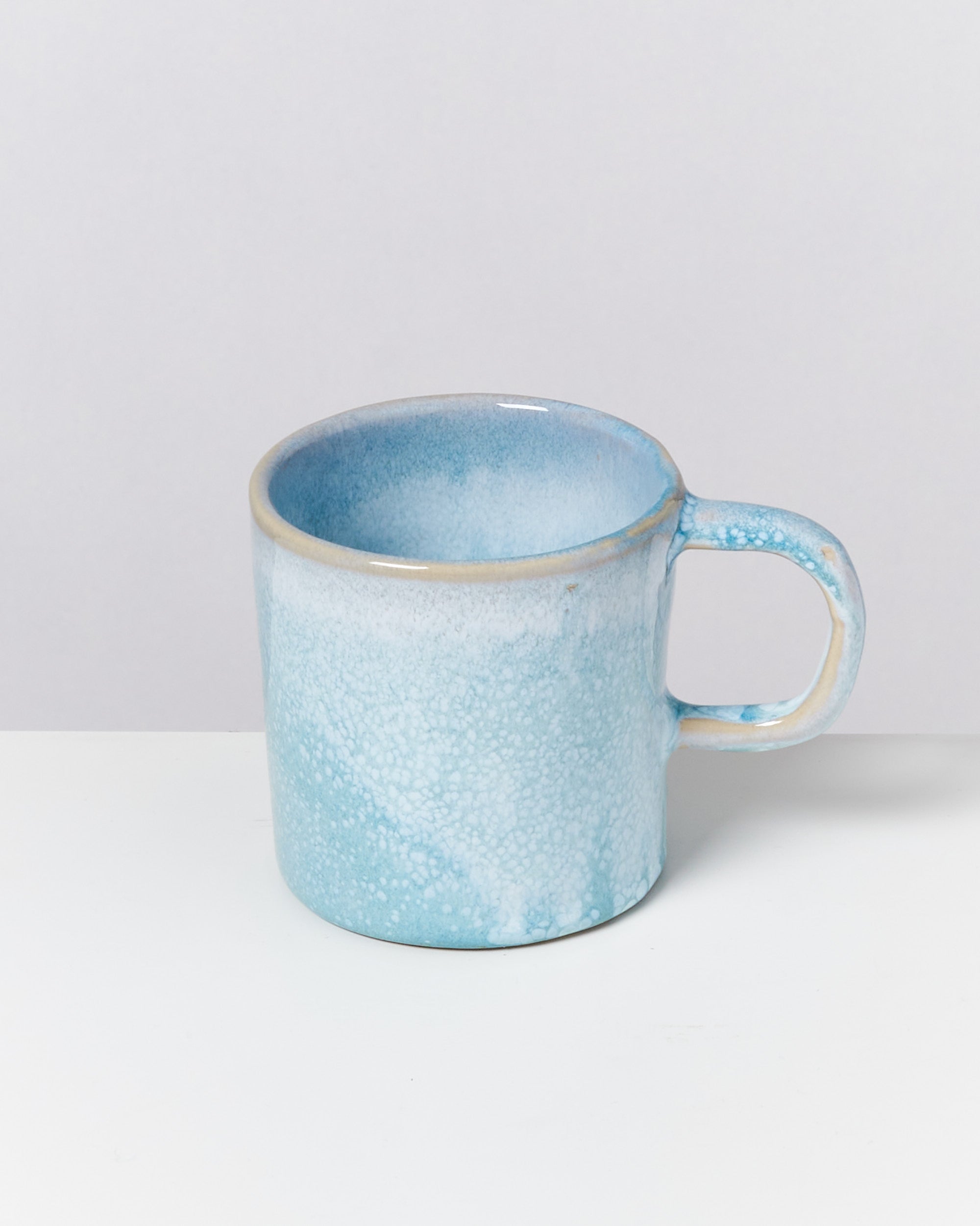 Hellblaue Keramiktasse mit Henkel auf einer weißen Oberfläche.