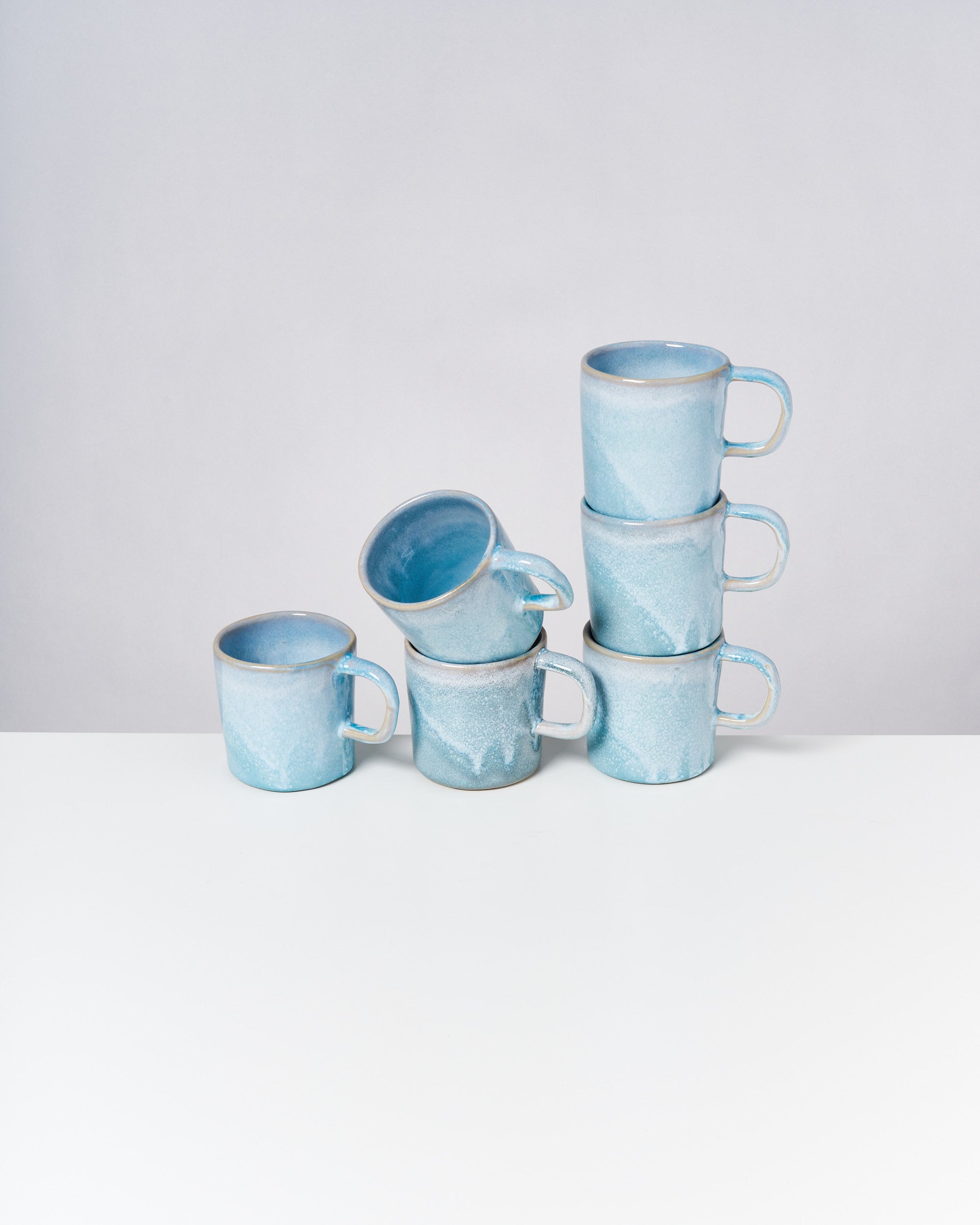 Sechs türkisfarbene Tassen sind auf einem Tisch gestapelt, zwei Tassen oben und vier unten im Stapel.