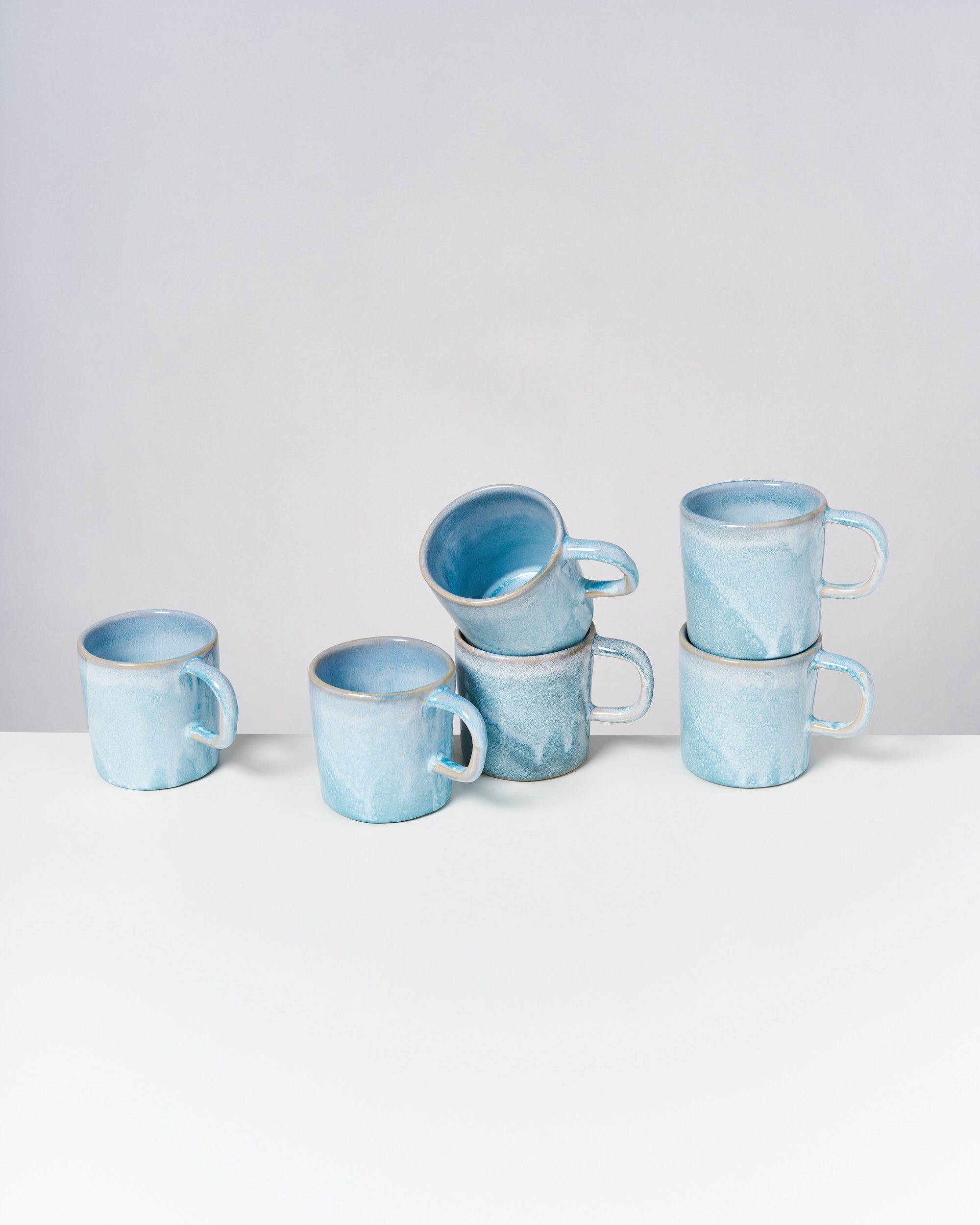 Sechs blaue Tassen mit Griffen sind auf einem Tisch arrangiert, wobei einige gestapelt sind.